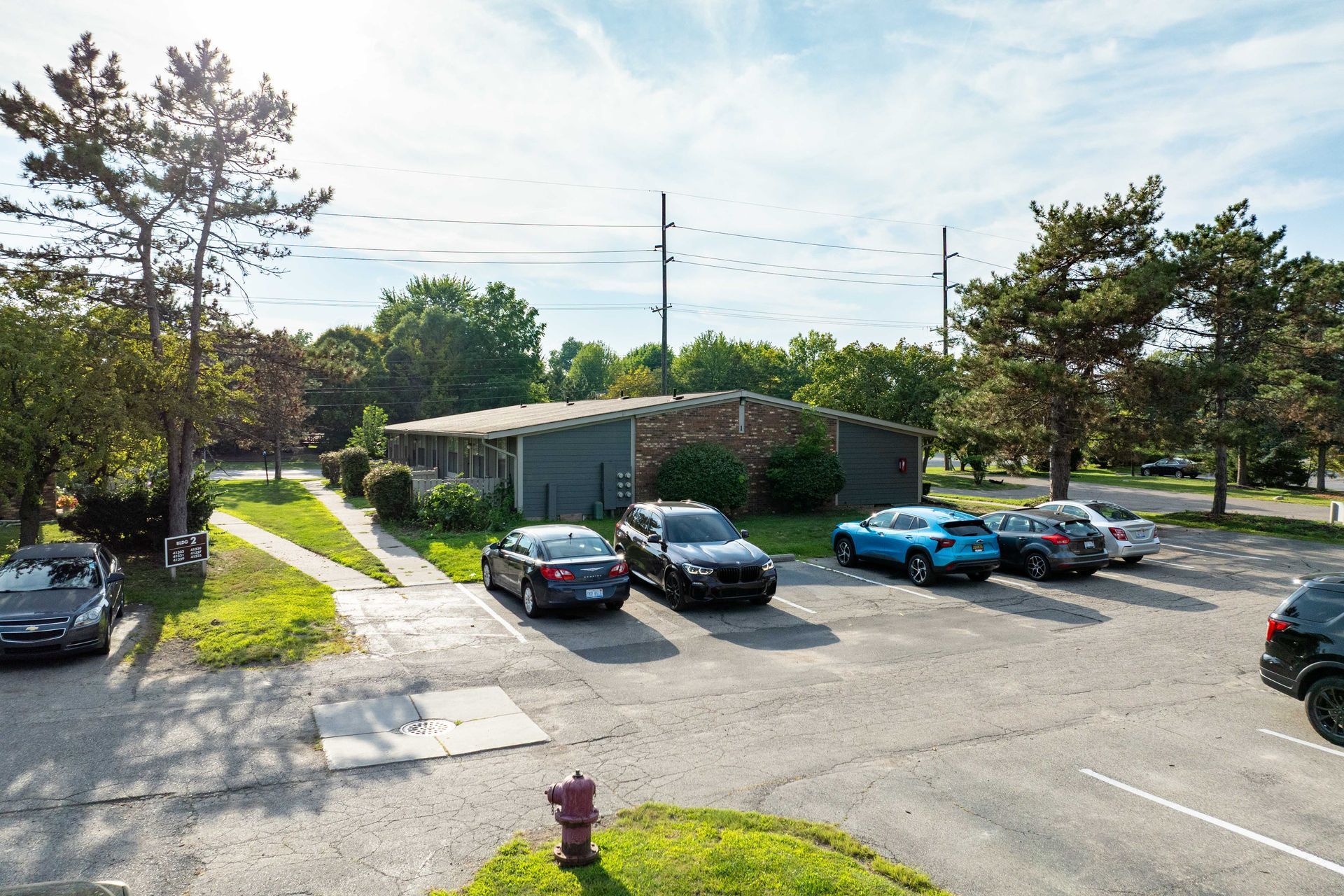 Parking lot with cars in front of a single-story building and trees.