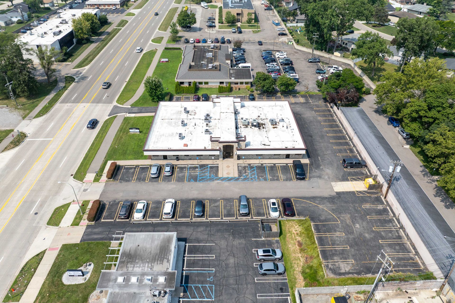 An aerial view of a building with a parking lot next to a road, cars are parked.