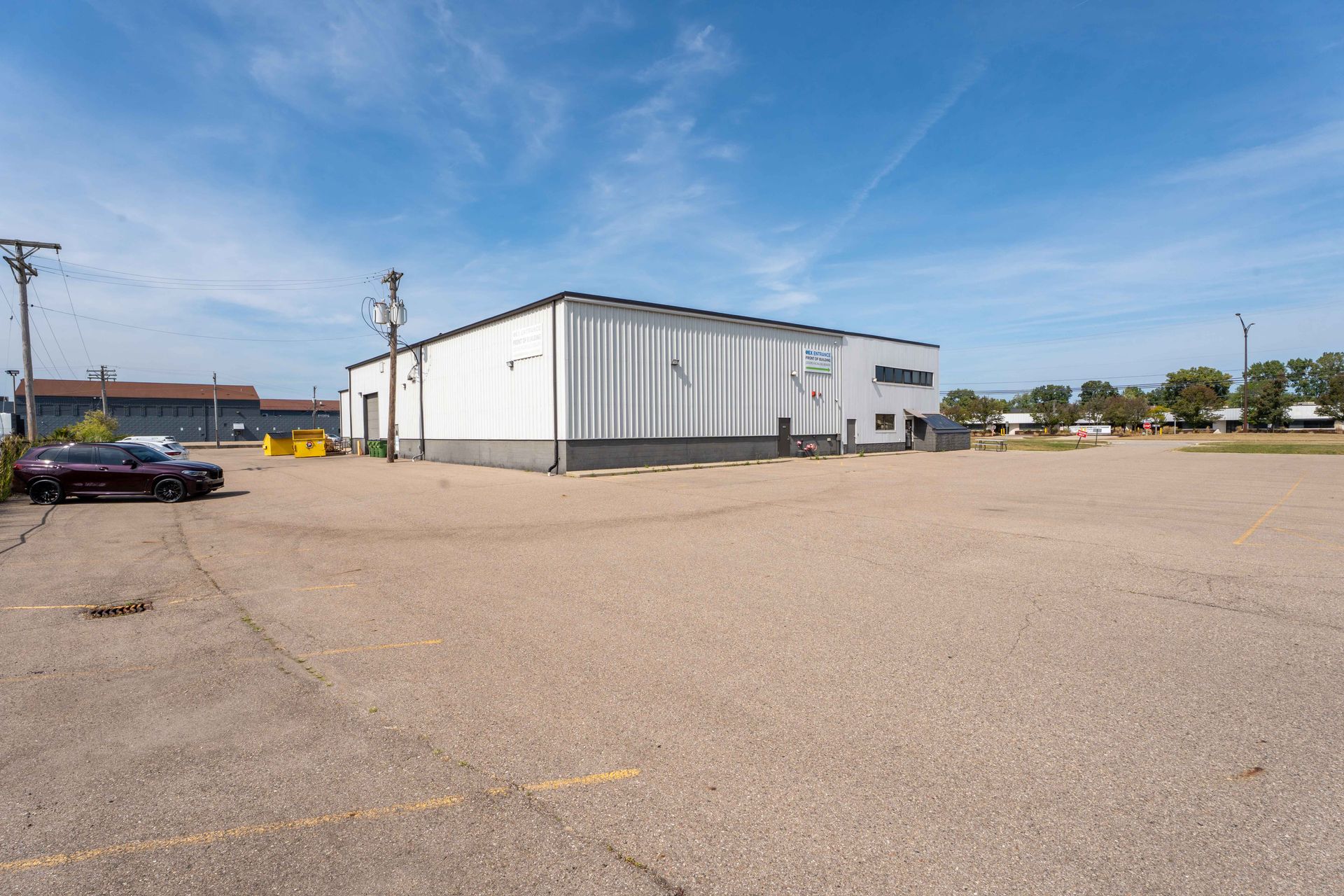 Large, white industrial building with paved parking lot under a blue sky.