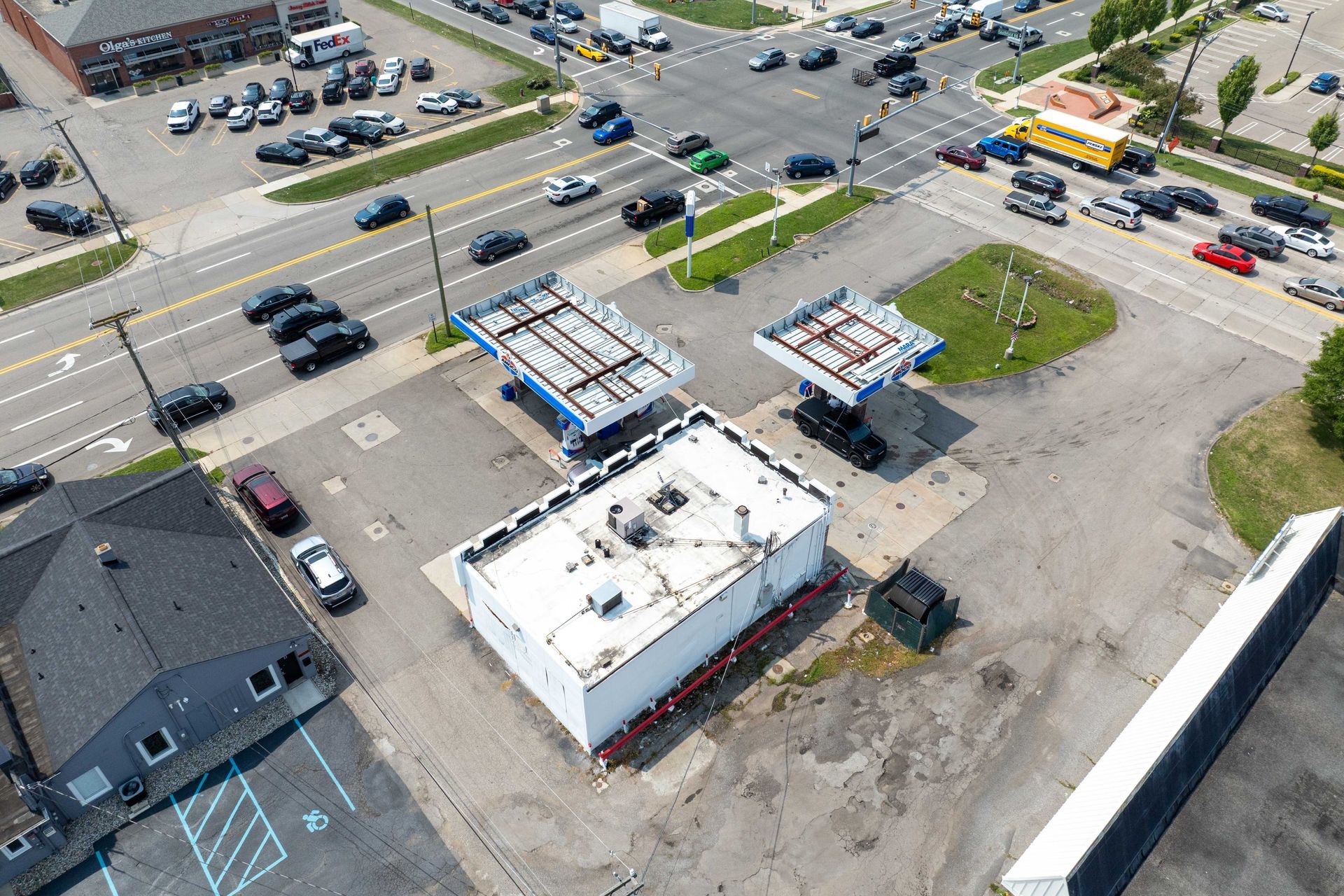 Aerial view of a gas station with empty pumps, a white building, and a busy intersection filled with cars.