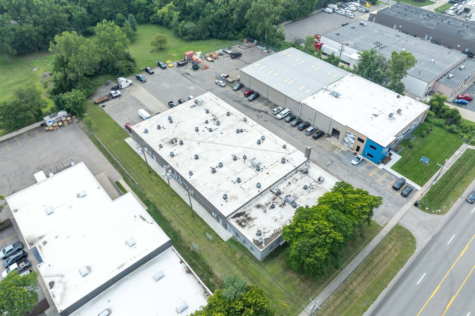 Aerial view of industrial buildings with cars parked outside on a sunny day.