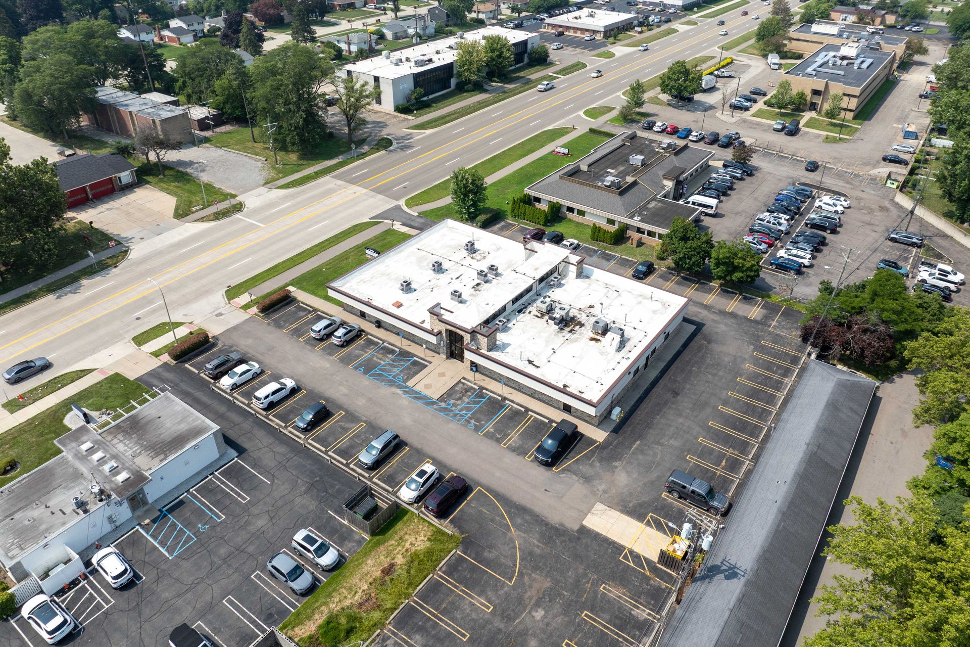 Aerial view of a commercial building with white roof, surrounded by parking lots and a road.