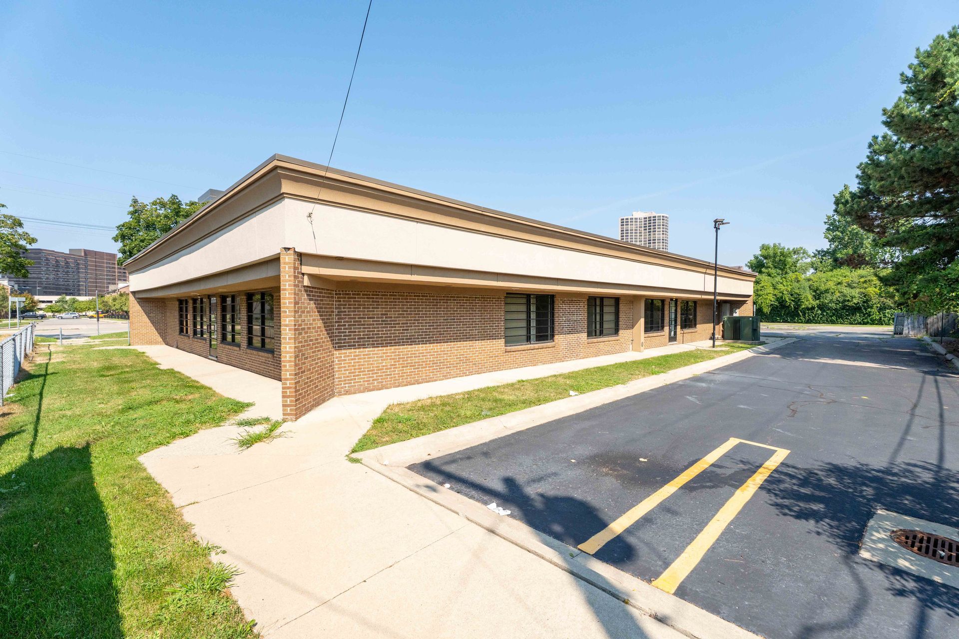 Commercial building with tan stucco and brick exterior, black windows, and a small asphalt parking area.