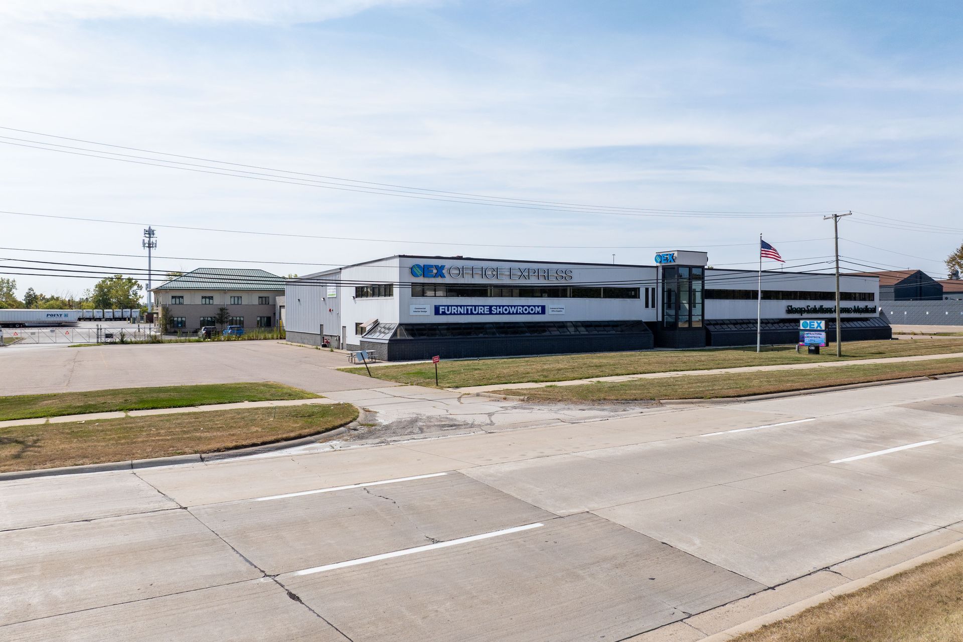 White and blue office building with an American flag. Road in foreground, blue sky.