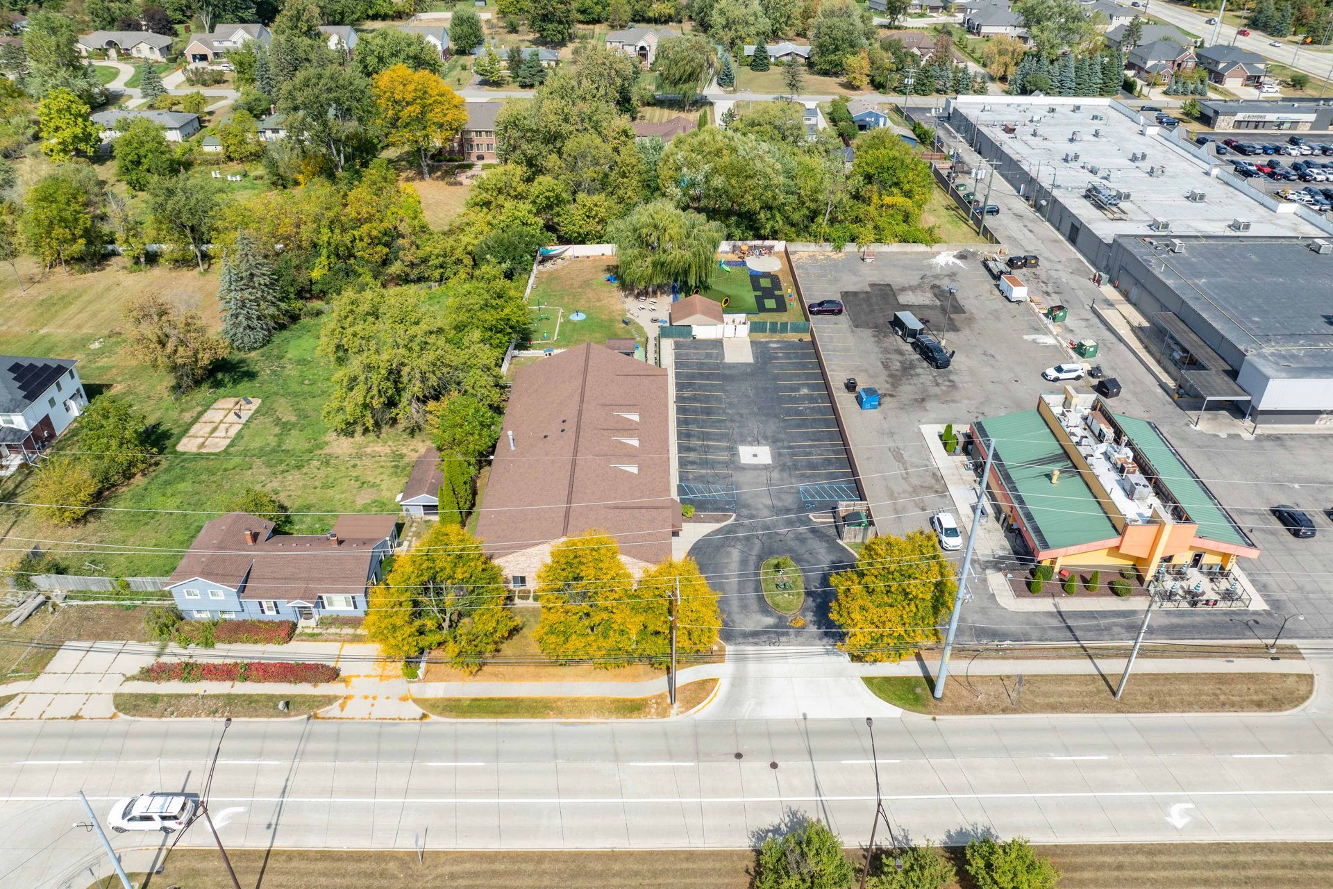Aerial view of commercial buildings with parking lots and surrounding greenery and a street in the foreground.