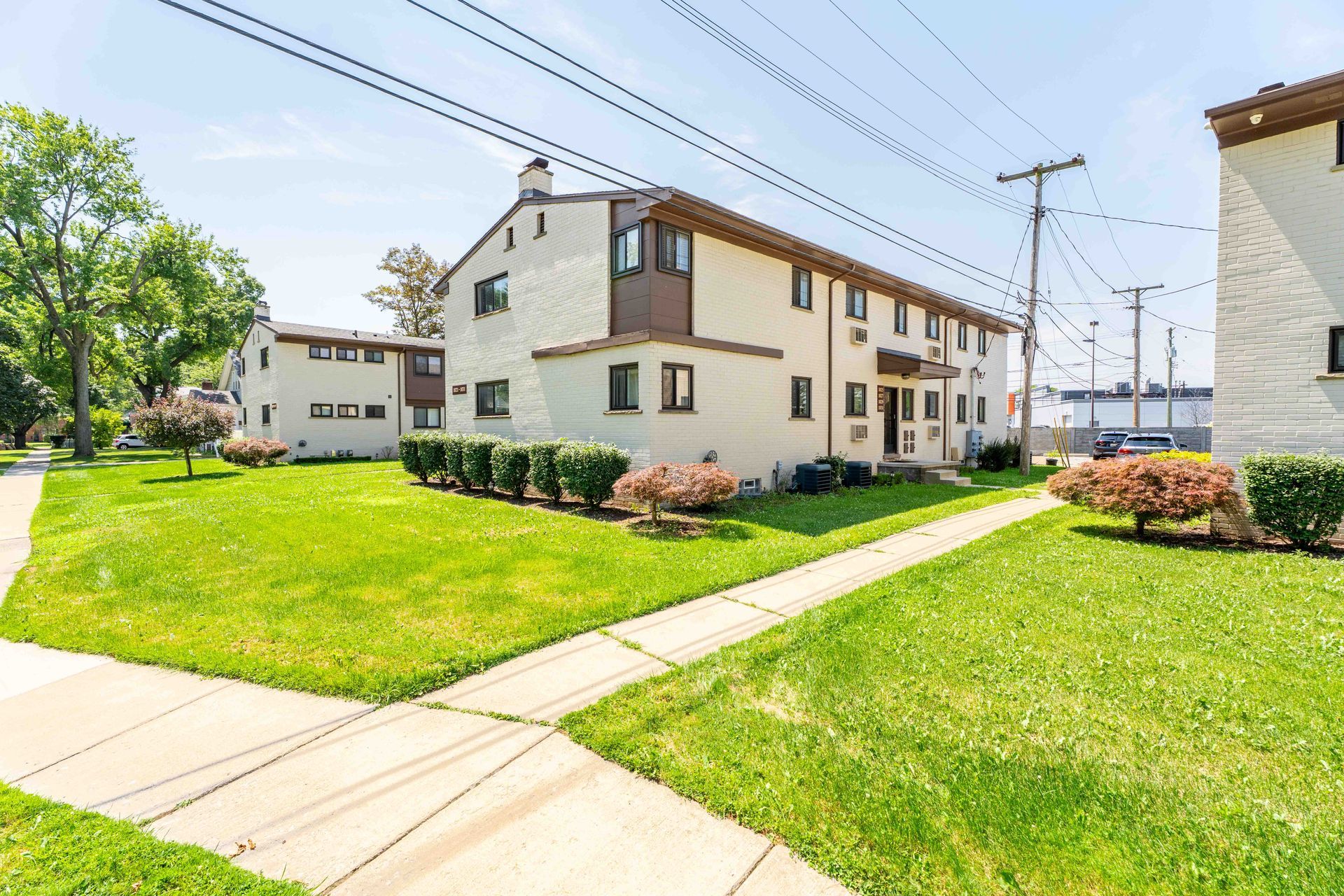 Two-story apartment buildings with brown trim, green lawns, sidewalk on sunny day.
