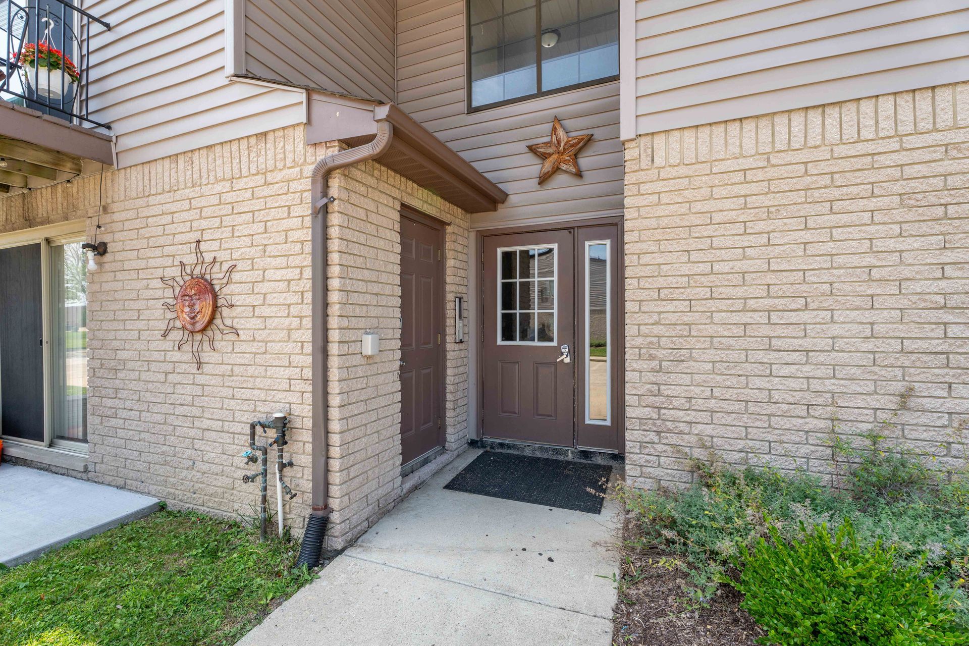 Beige brick exterior with brown door, Texas star, walkway, and greenery.