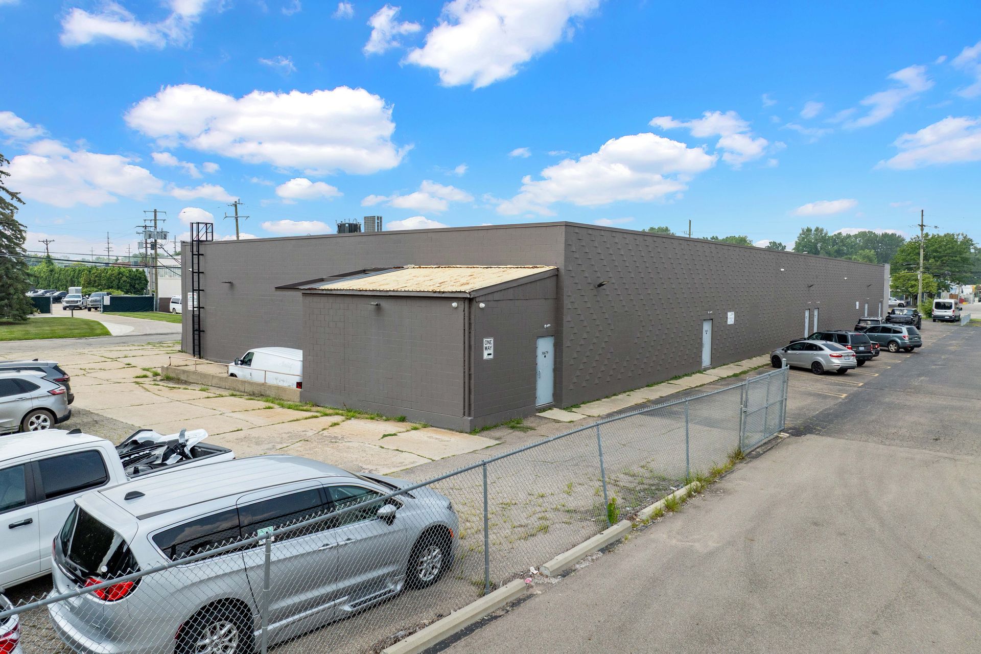 Exterior of a brown industrial building with parked cars on a sunny day.