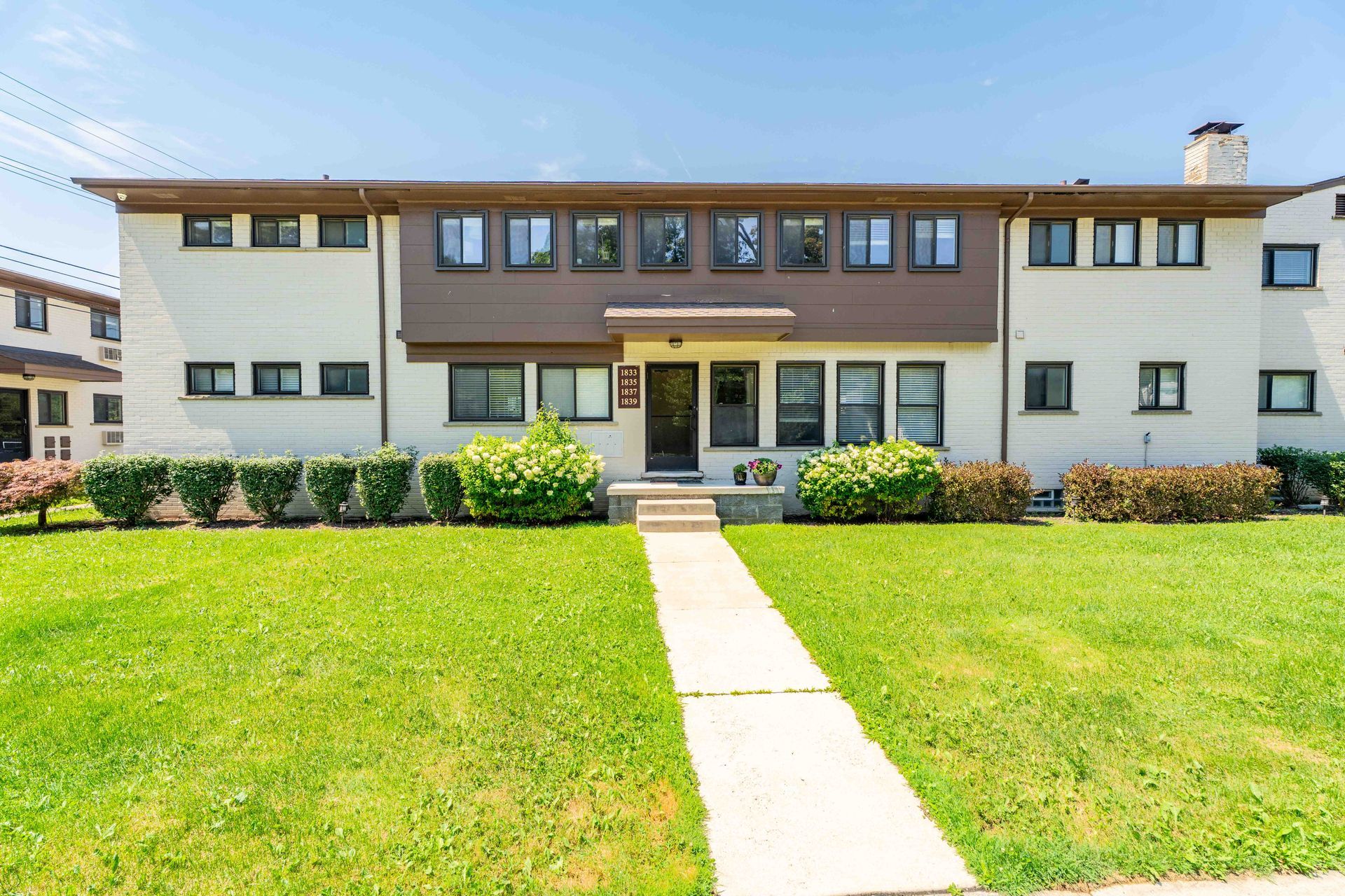 Apartment building with brown trim, centered walkway through green lawn, blue sky.