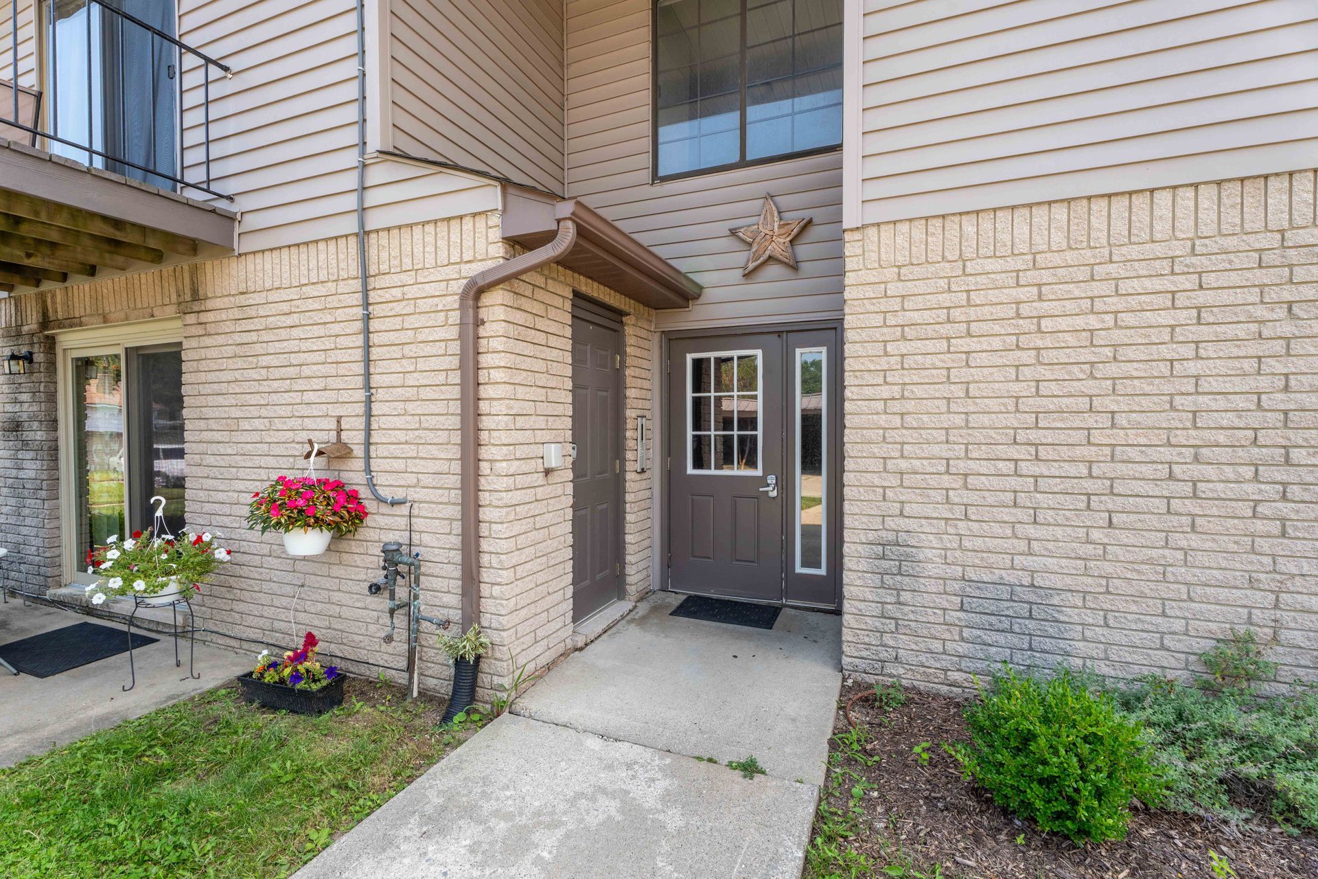 Tan brick apartment exterior with brown door, entryway, and small landscaping.