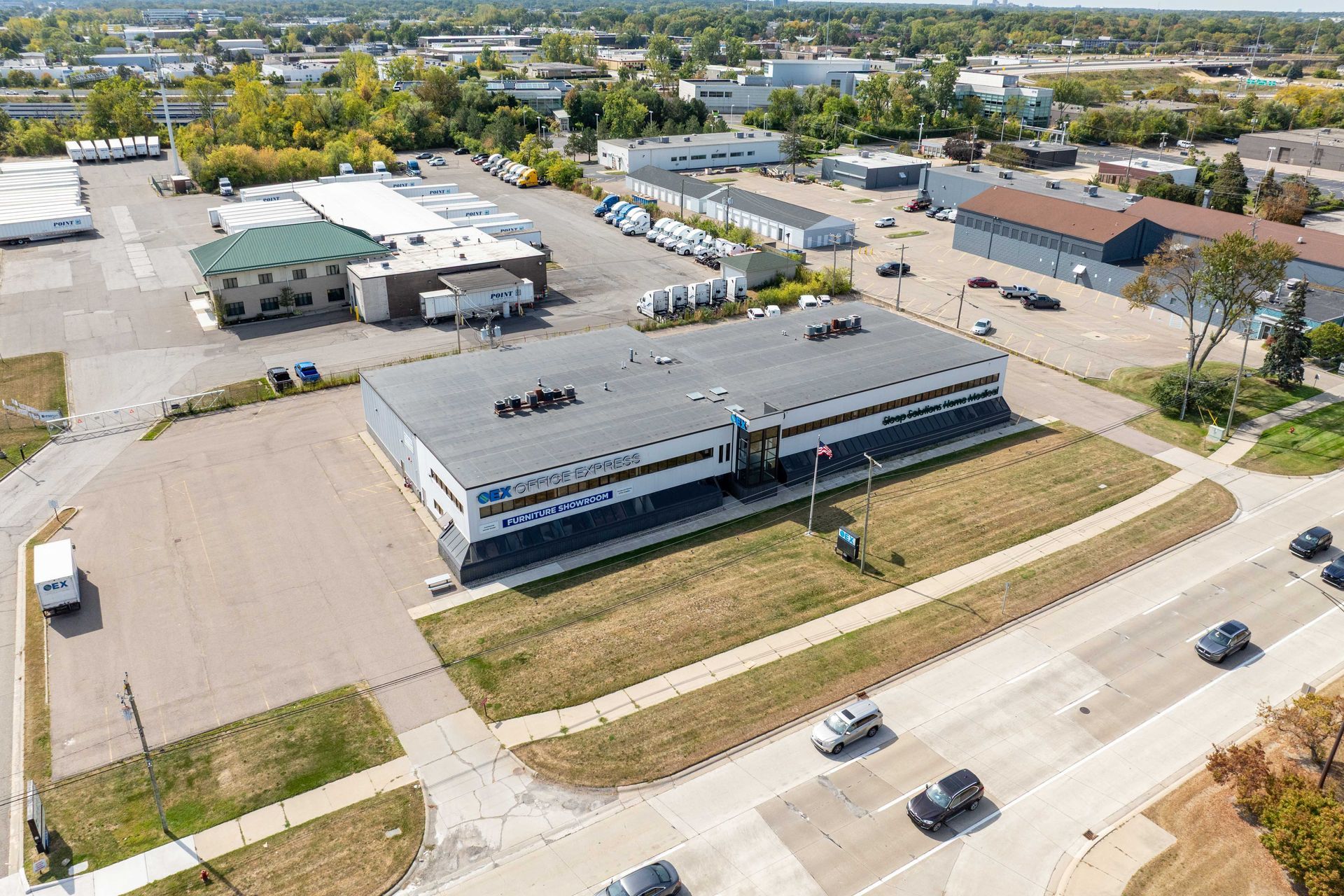 Aerial view of a commercial building with a long, gray roof and blue and white signage near a busy road.