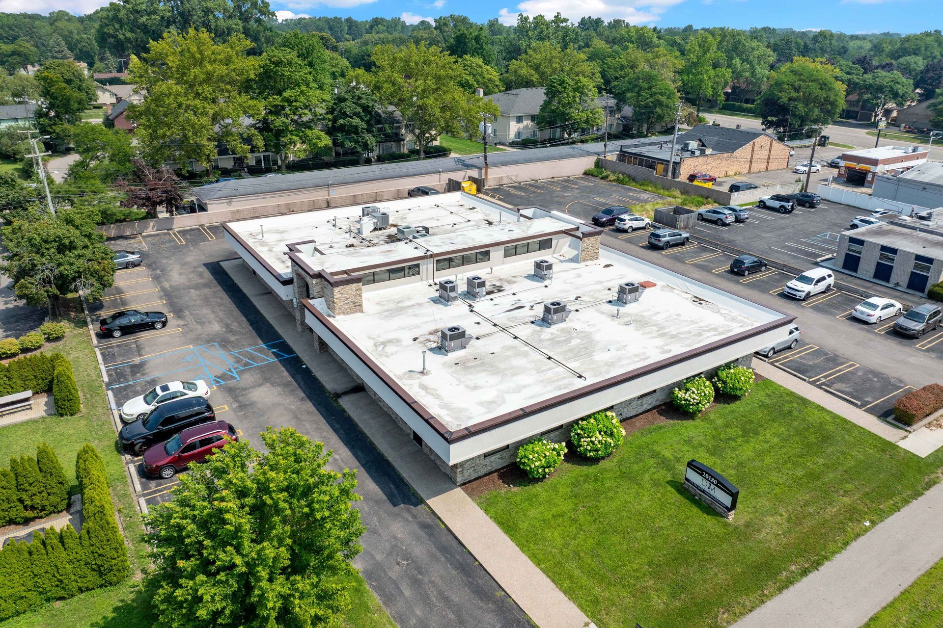 Aerial view of a low, rectangular building with a flat roof, surrounded by parking lots and trees.