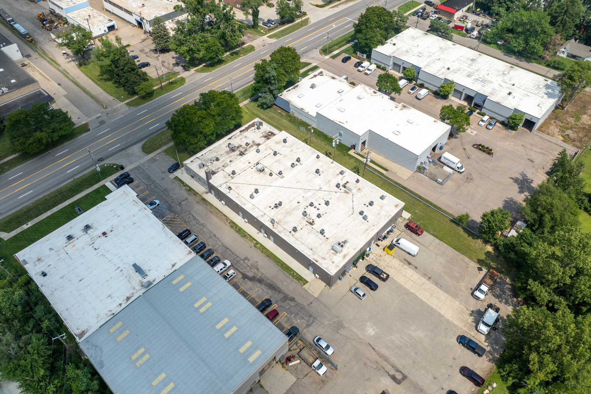 Aerial view of industrial buildings with white roofs, a parking lot, and a road.