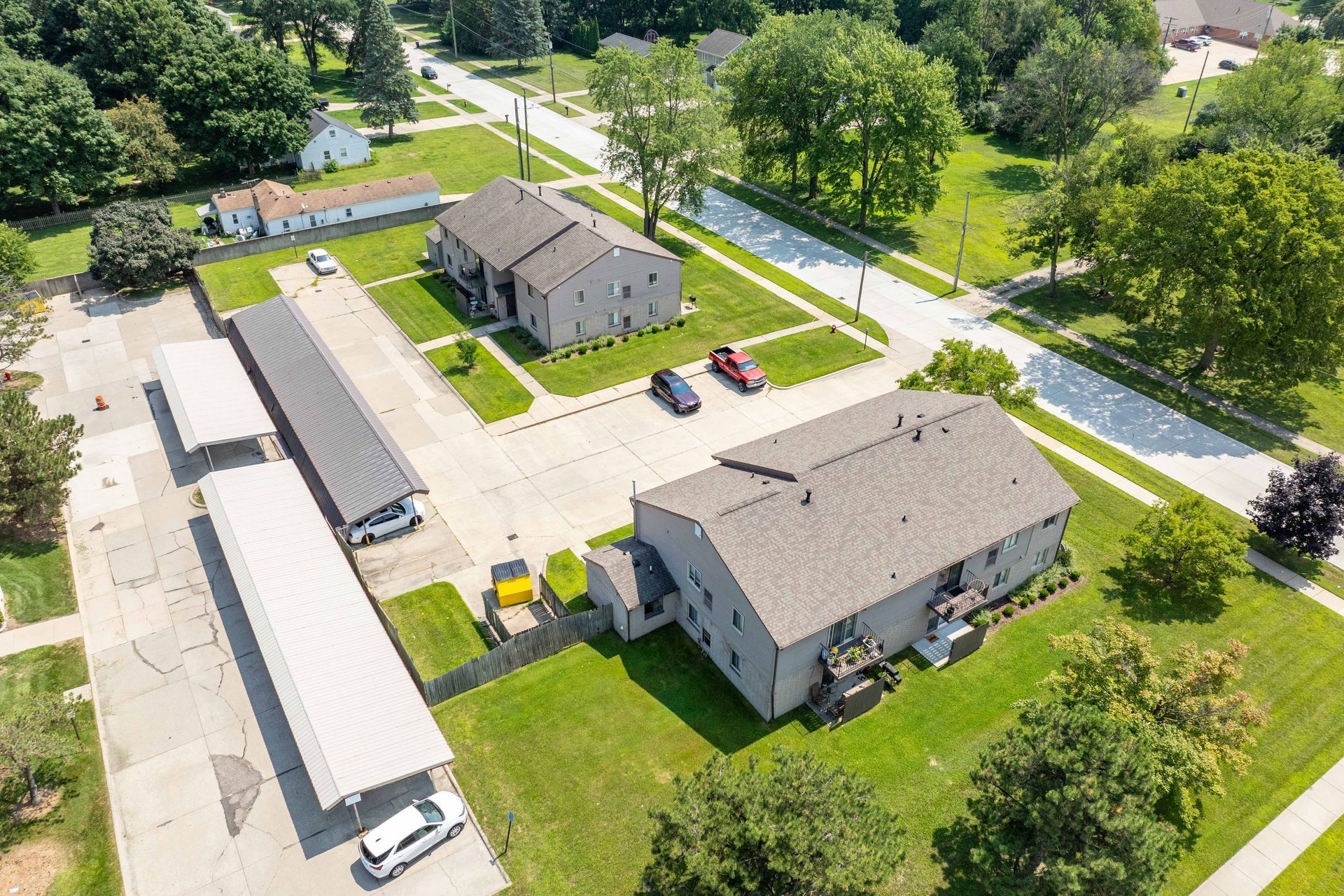 Aerial view of apartment buildings with covered parking, green lawns, and trees.
