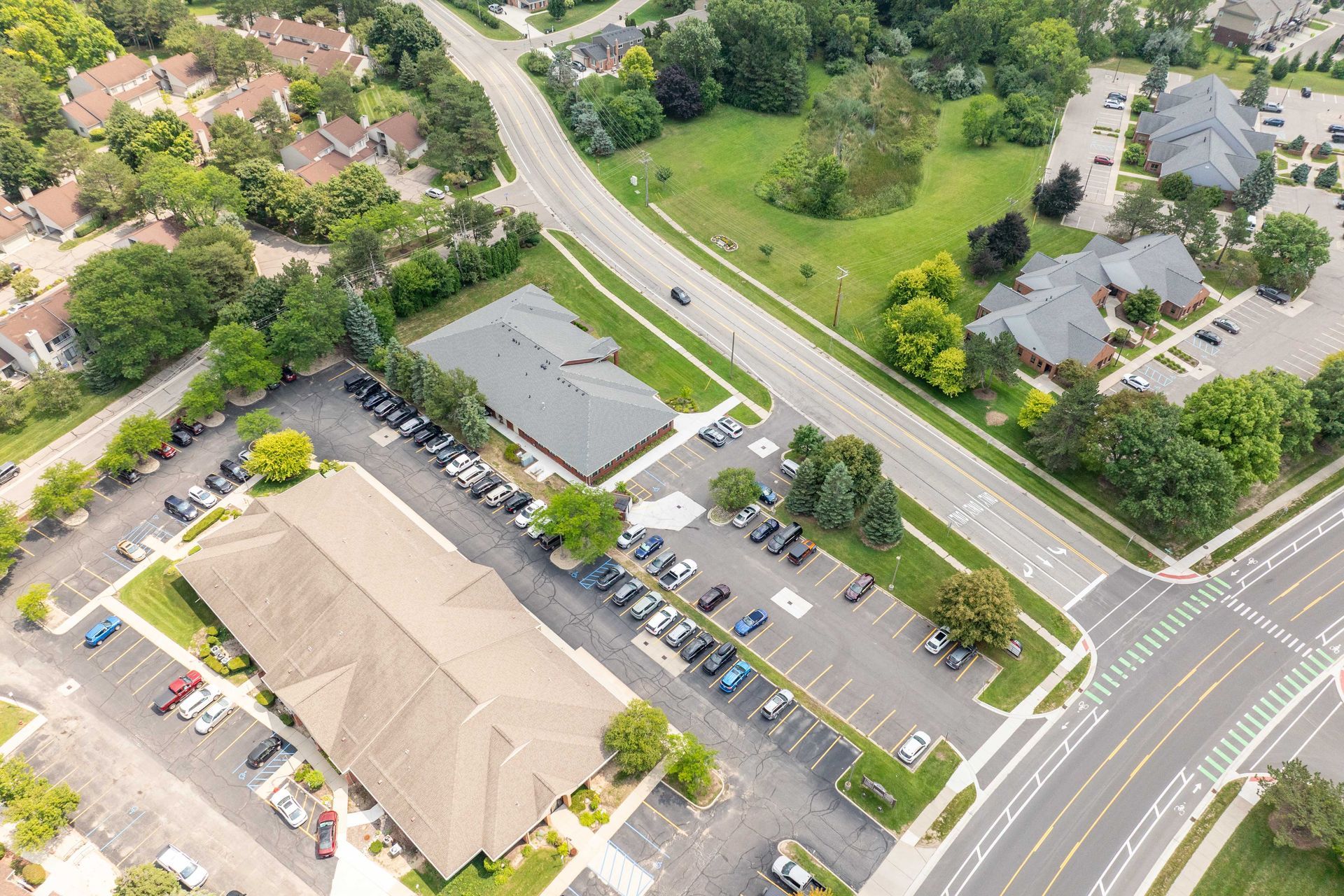 Aerial view of buildings, roads, and parking lots surrounded by green trees and grass.