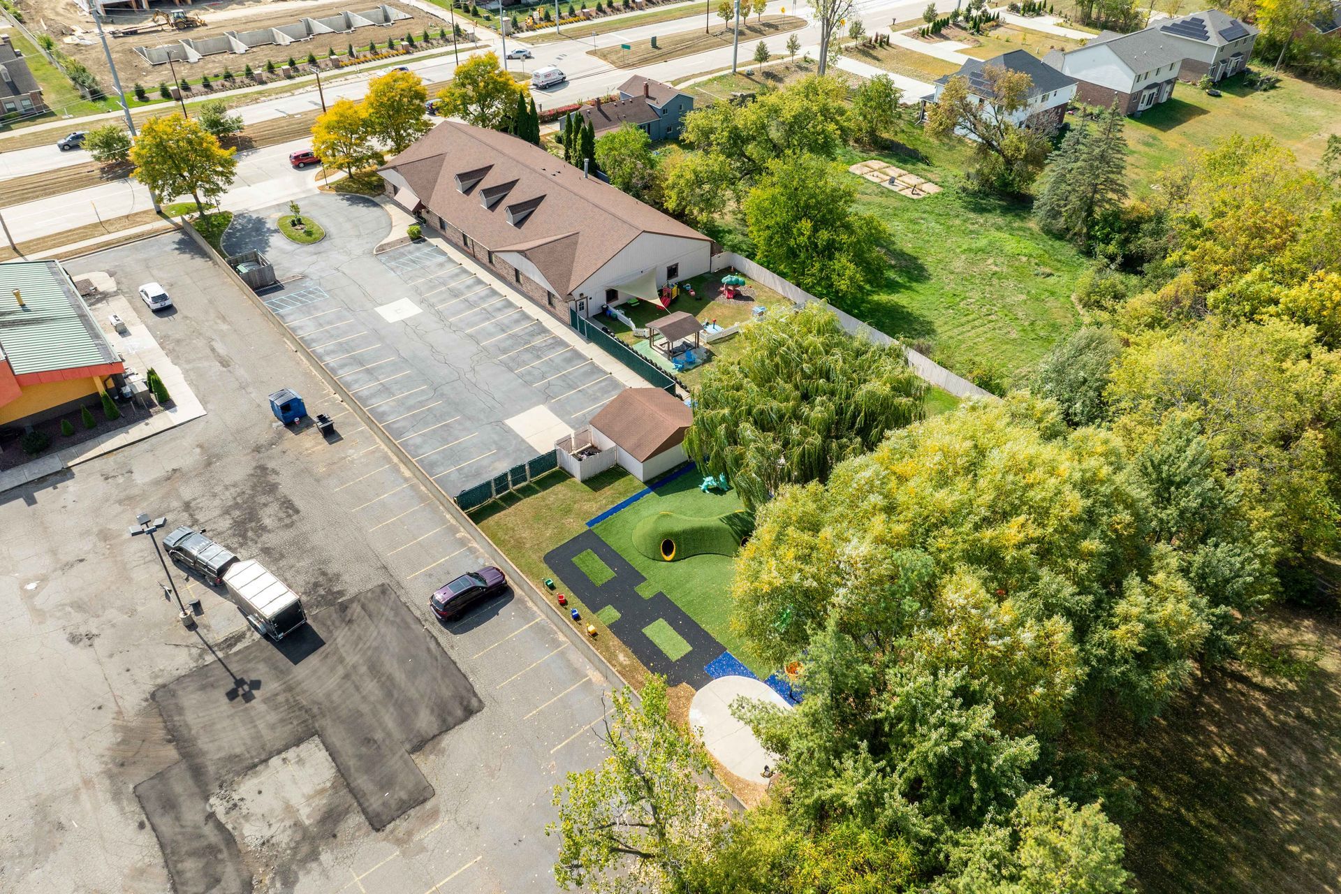 Aerial view: building with tan roof and multiple parking lots surrounded by trees and grass.