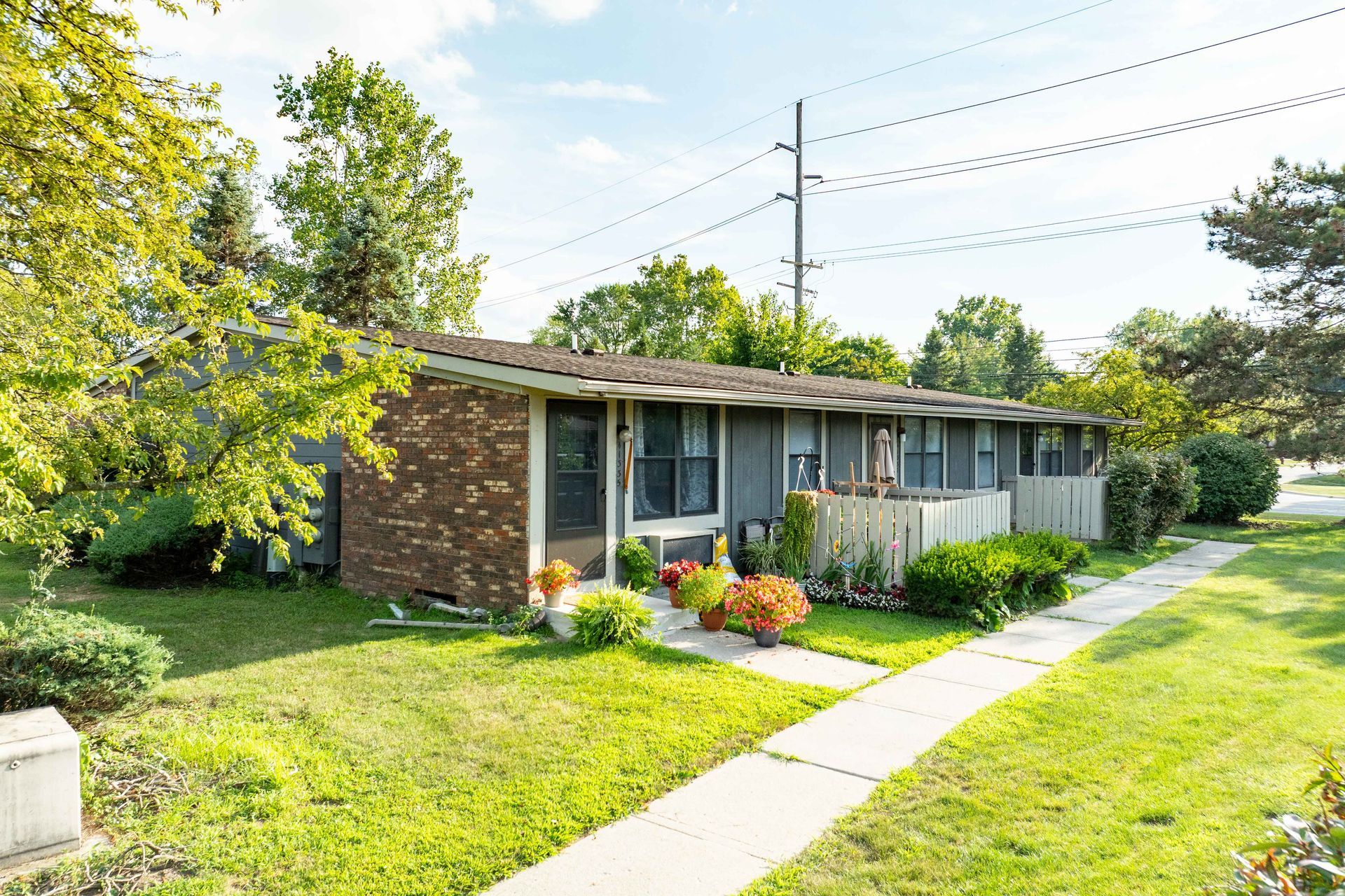 Low-rise apartment building with brick facade, surrounded by green grass, walkway, and trees under a blue sky.