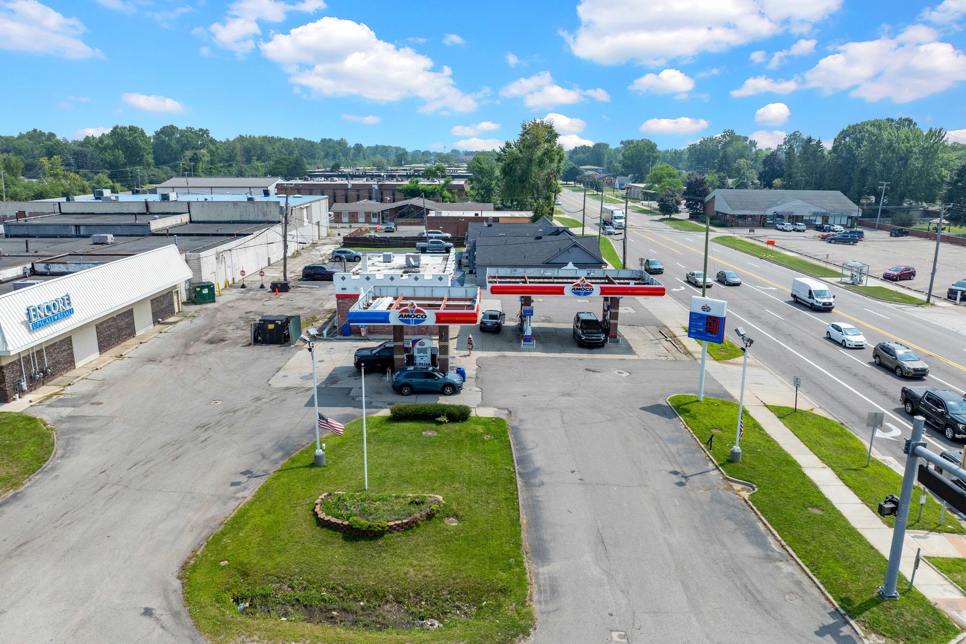 Aerial view of a gas station with cars, a street, and surrounding buildings on a sunny day.