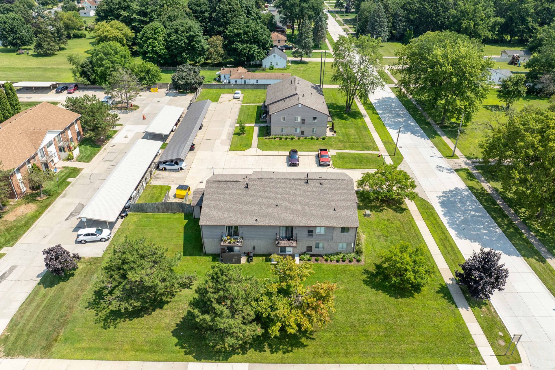 Aerial view of apartment buildings with parking and green lawns in a residential area.