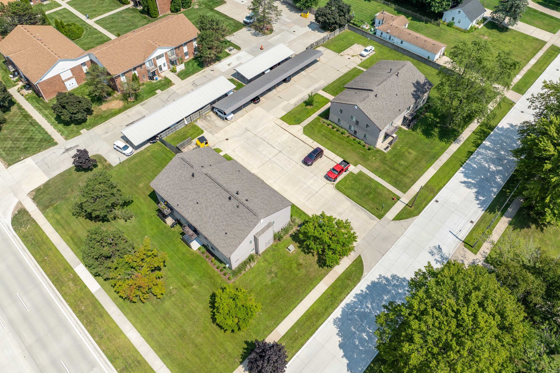 Aerial view of several buildings and parking, with green lawns, trees, and cars.