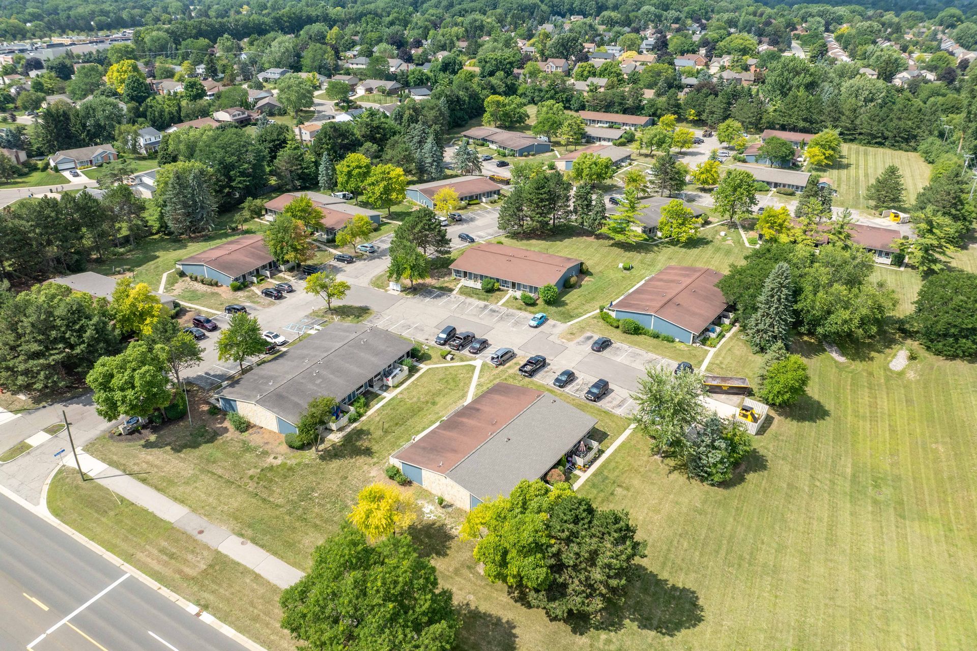 Aerial view of low-rise buildings with brown roofs, green trees, and parking spaces.