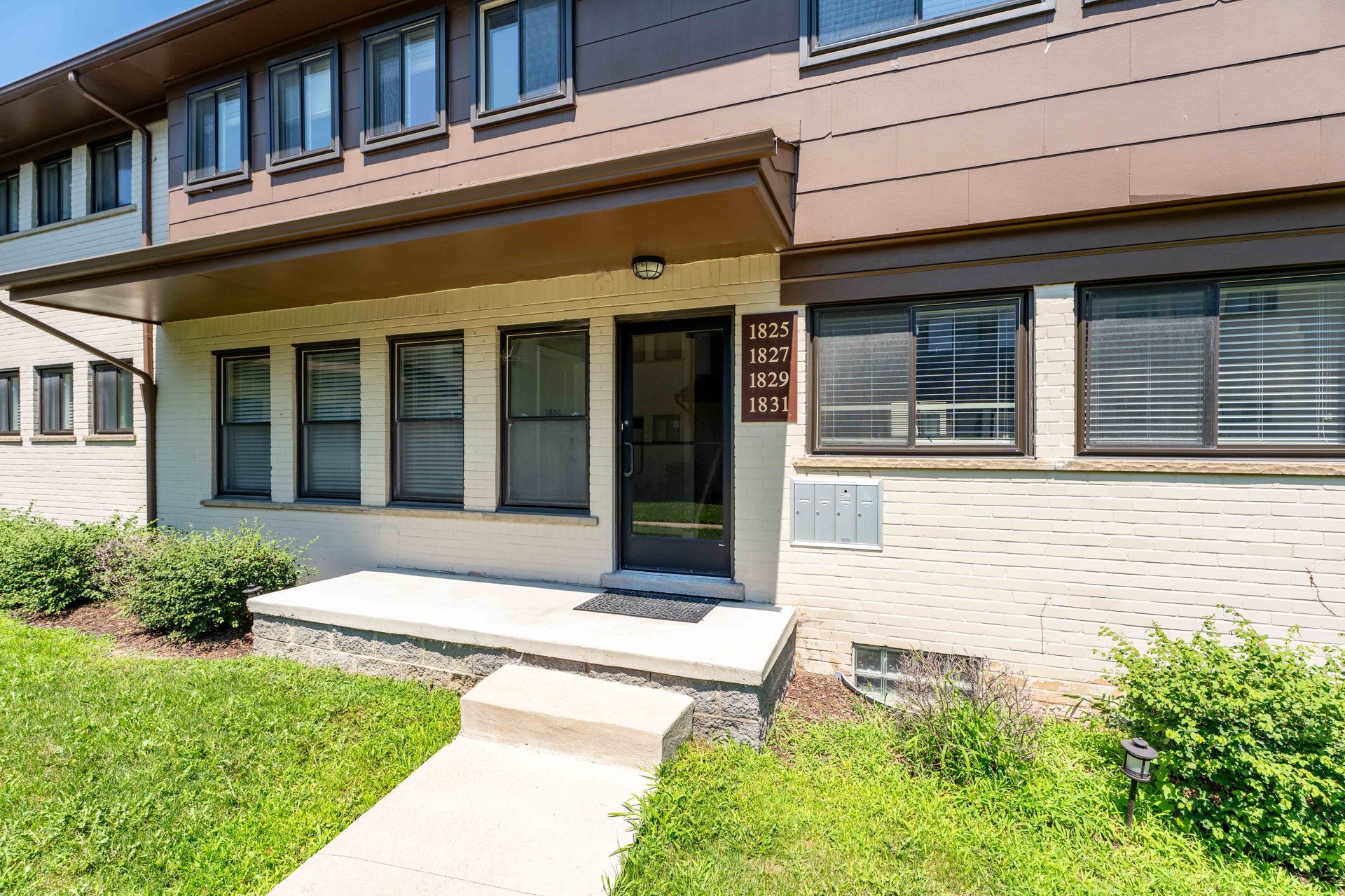 Row of townhouses with brown and beige siding, a front door, and a small stoop.
