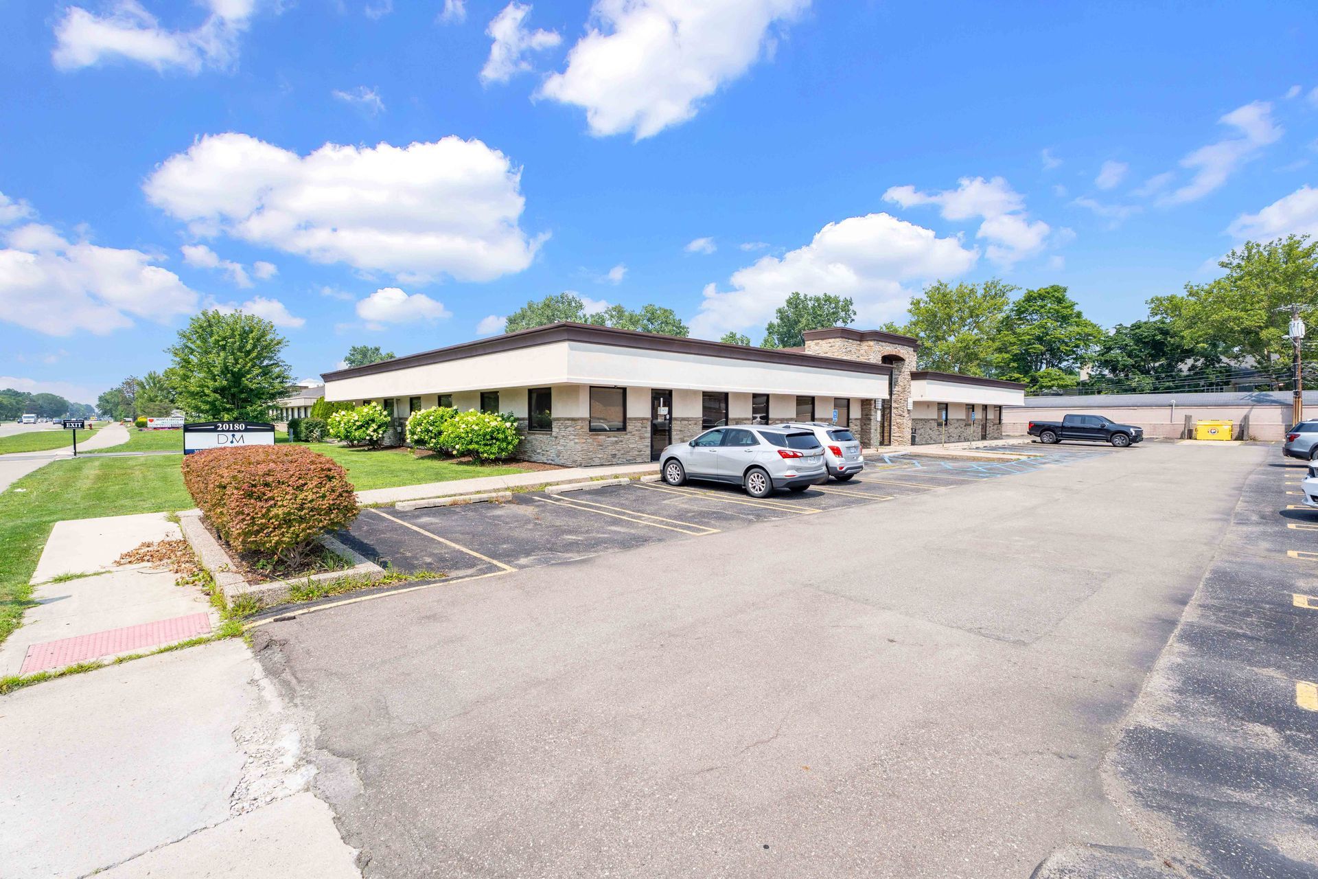 Commercial building with paved parking lot, parked cars, shrubs, and a clear, blue sky.