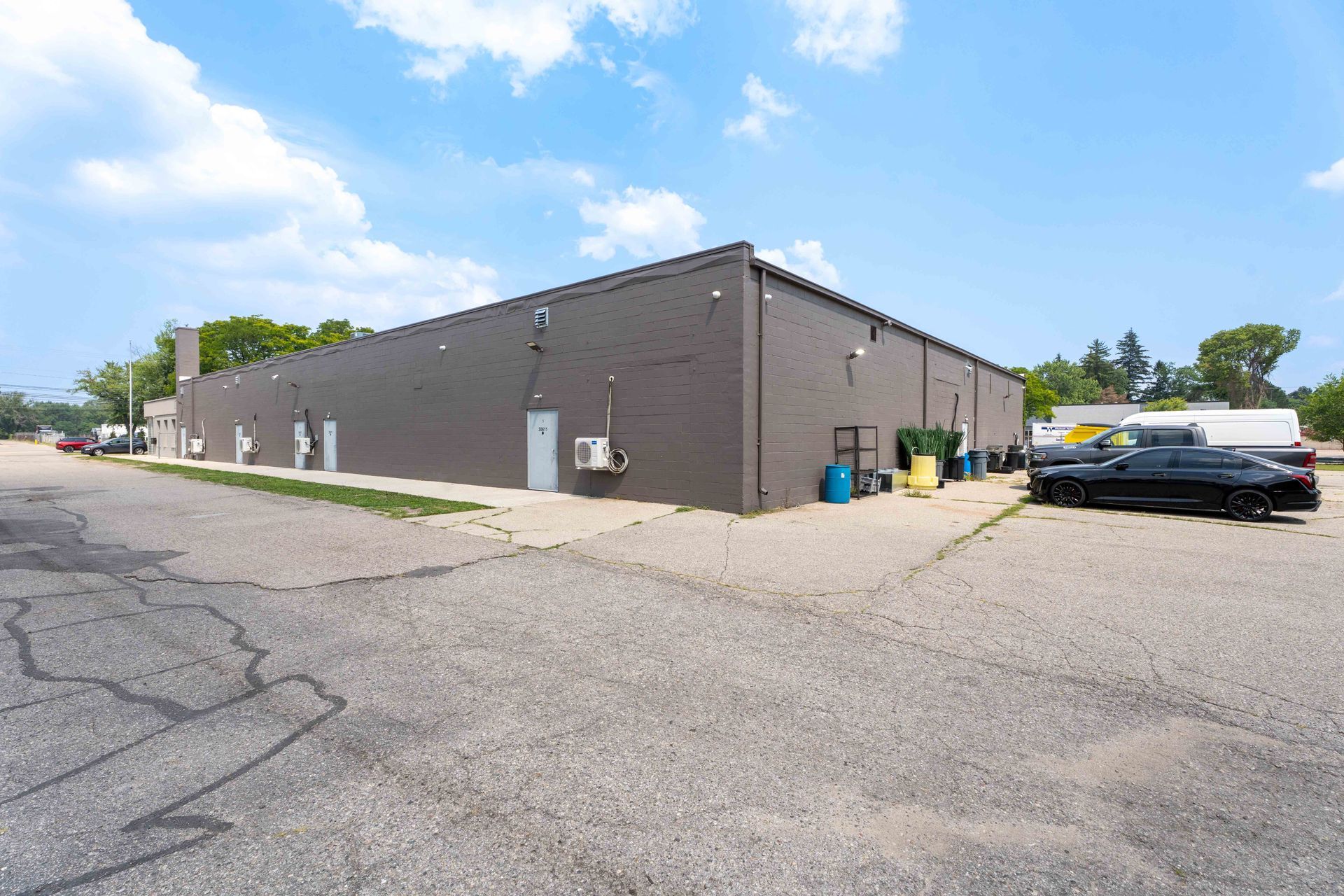 Gray commercial building with a large parking area under a blue sky.