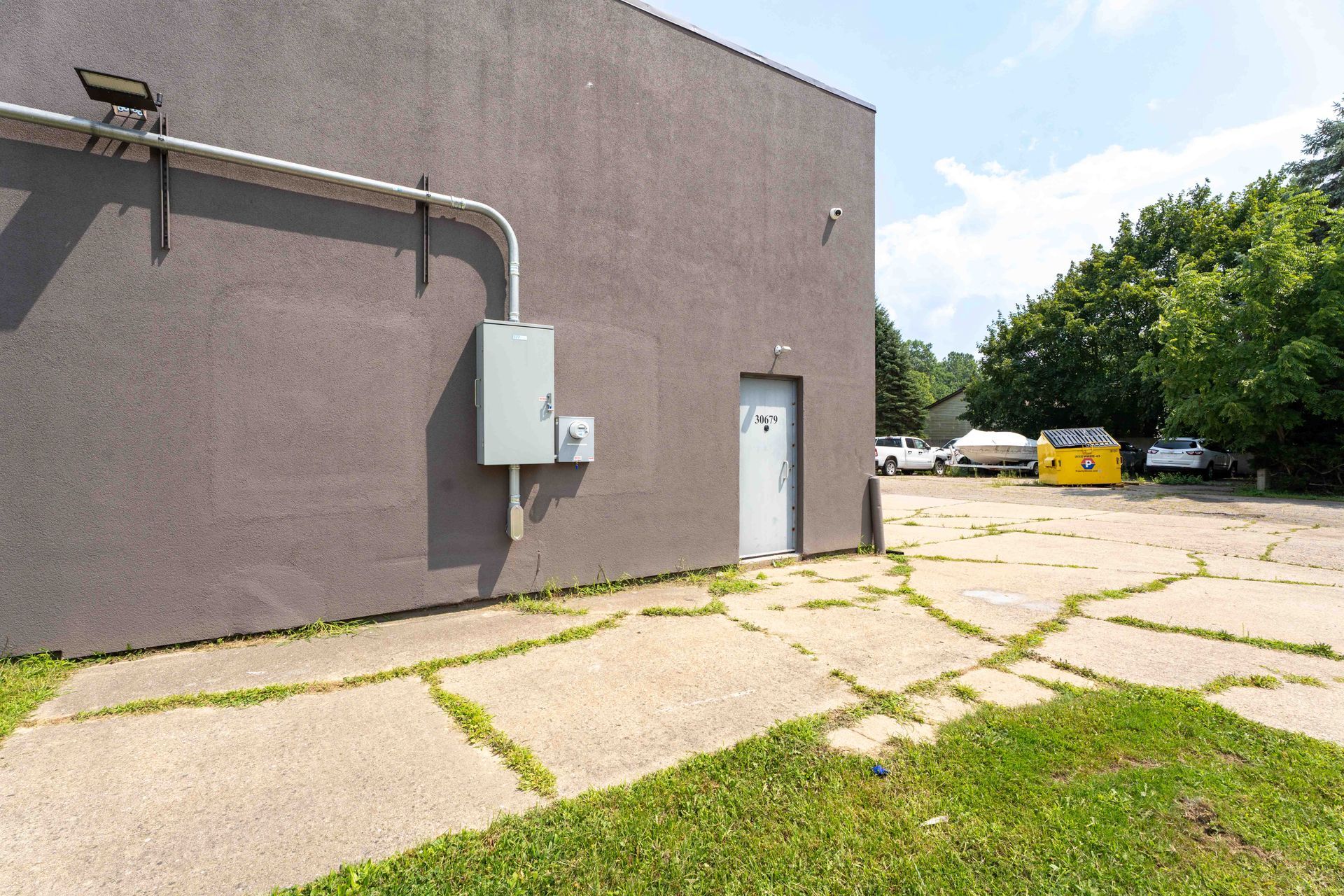 Exterior view of a building with a gray exterior, a door, and a concrete lot with grass.
