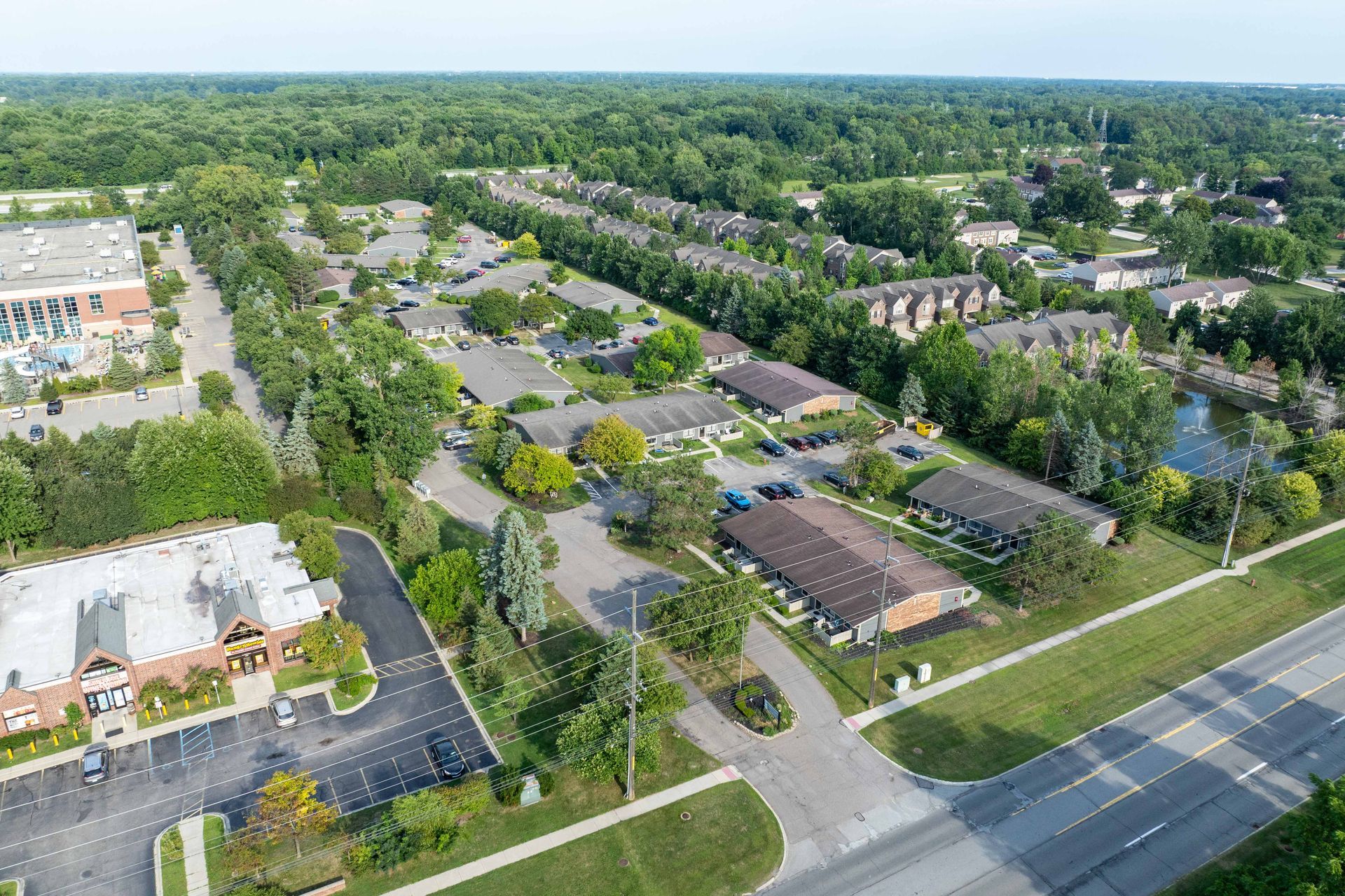Aerial view of a suburban neighborhood with buildings, trees, roads, and a parking lot on a sunny day.