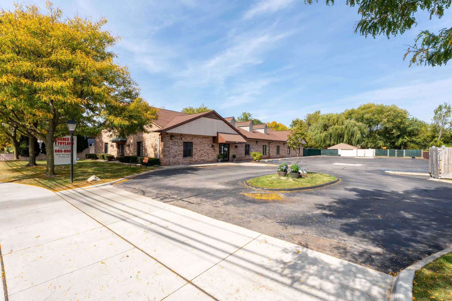 Brick building with brown roof, large parking lot, and trees under a blue sky.