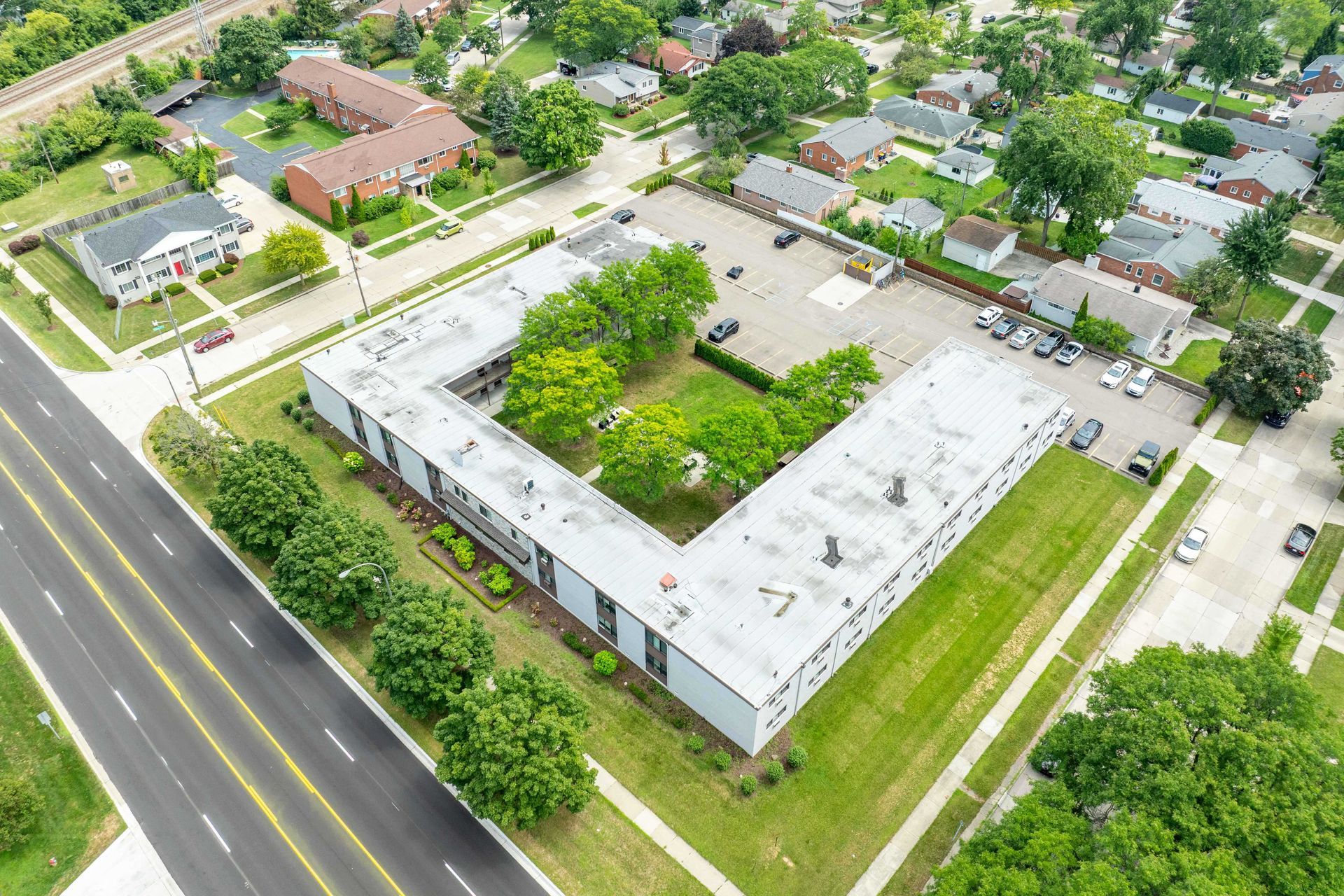 Aerial view of U-shaped white building with green courtyard, surrounded by roads and houses.