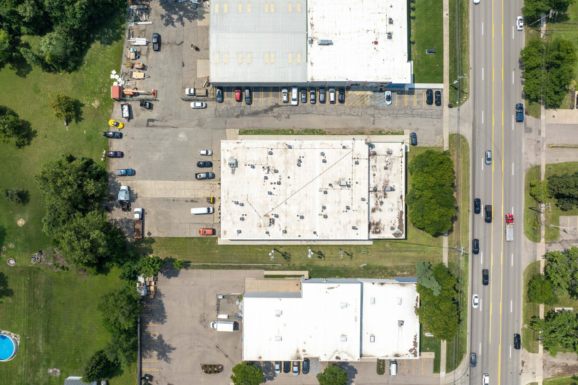 Aerial view of commercial buildings, parking lots, a road with traffic, and green spaces.
