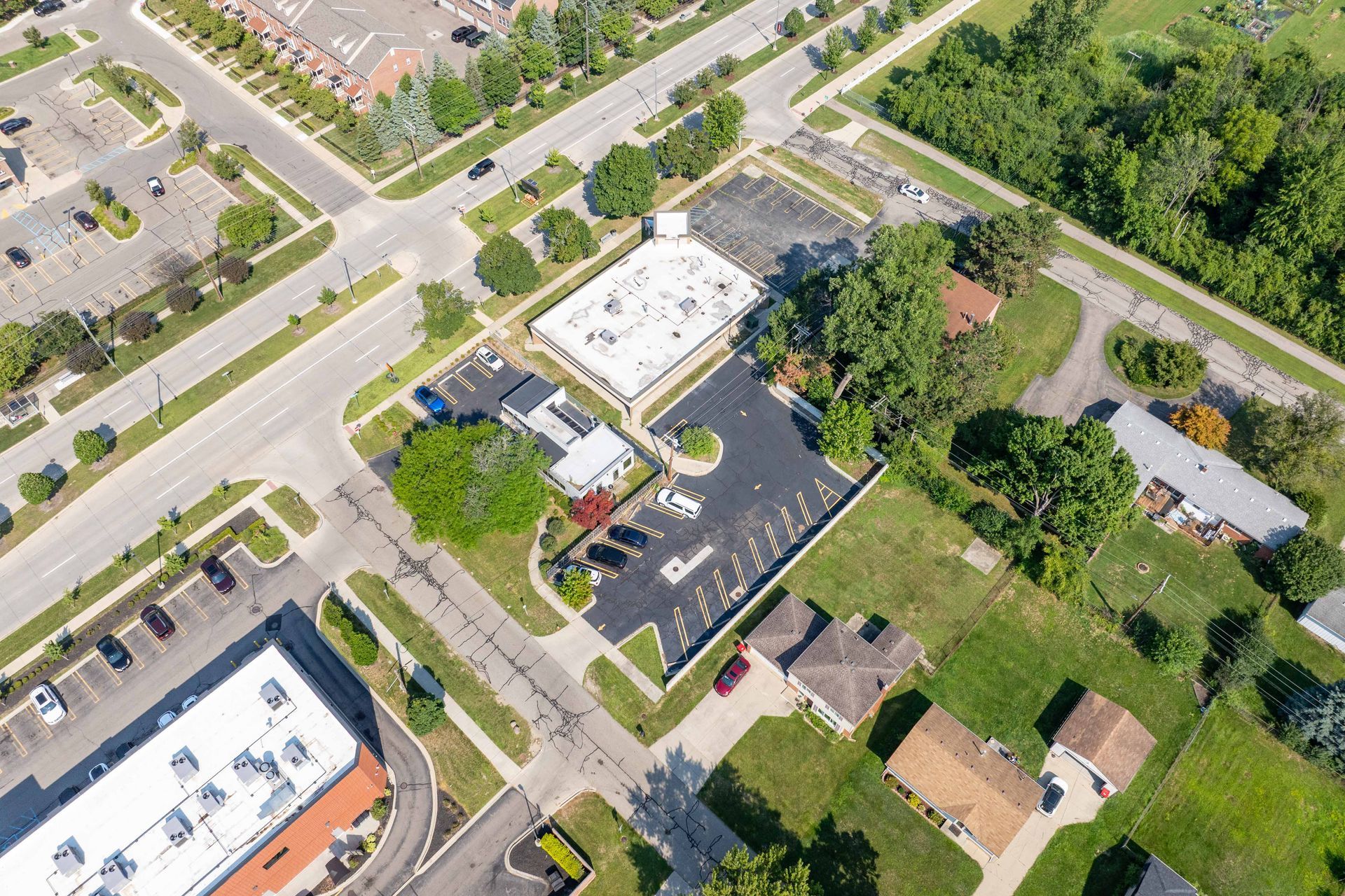 Aerial view: commercial building with parking lot and surrounding residential area near a street intersection.