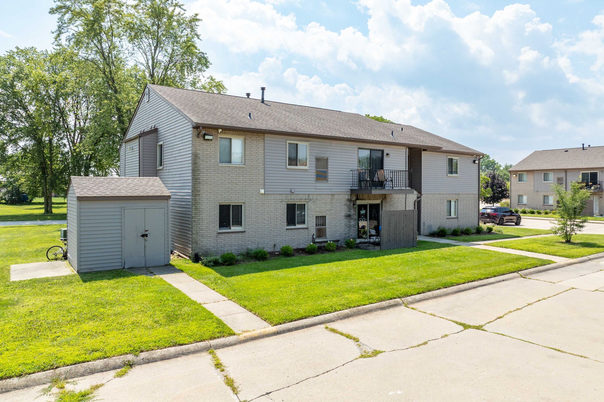 Gray two-story apartment building with a storage shed in front, green lawn and a blue sky.
