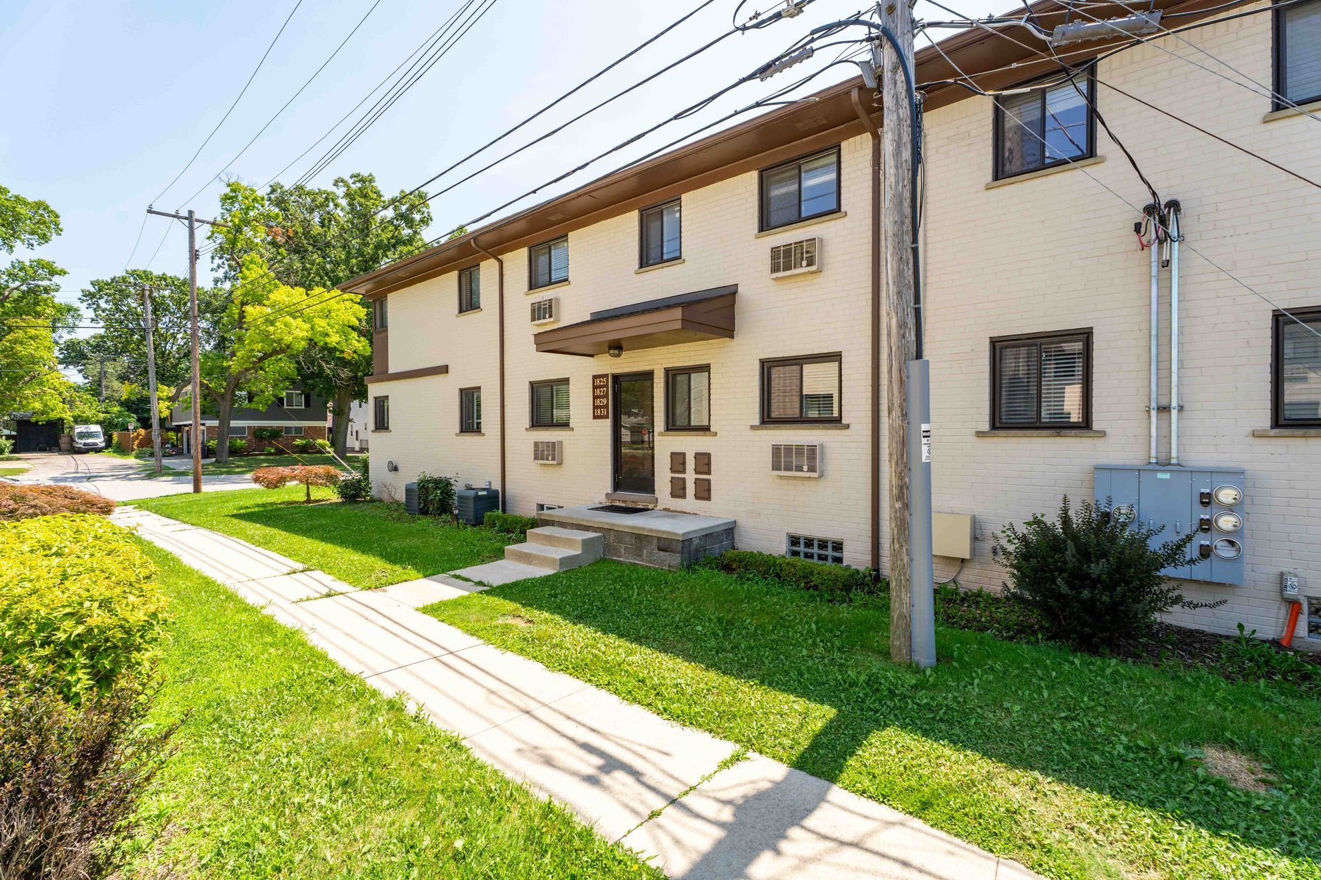 Two-story beige apartment building with walkway, grass lawn, and bright blue sky.