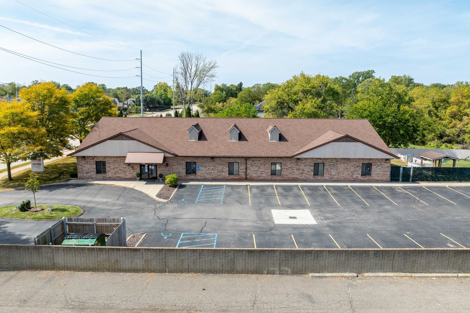 Brick building with brown roof and large parking lot on a sunny day.