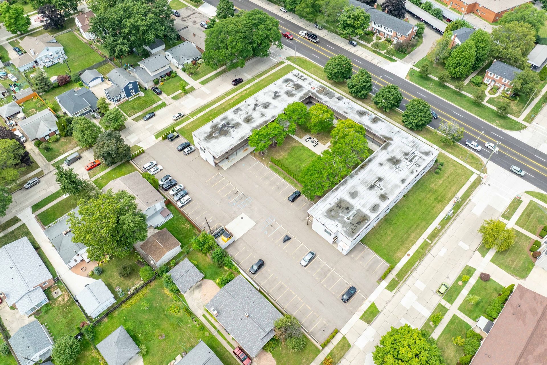 Aerial view of an L-shaped apartment complex with parking, surrounded by green lawns and streets.