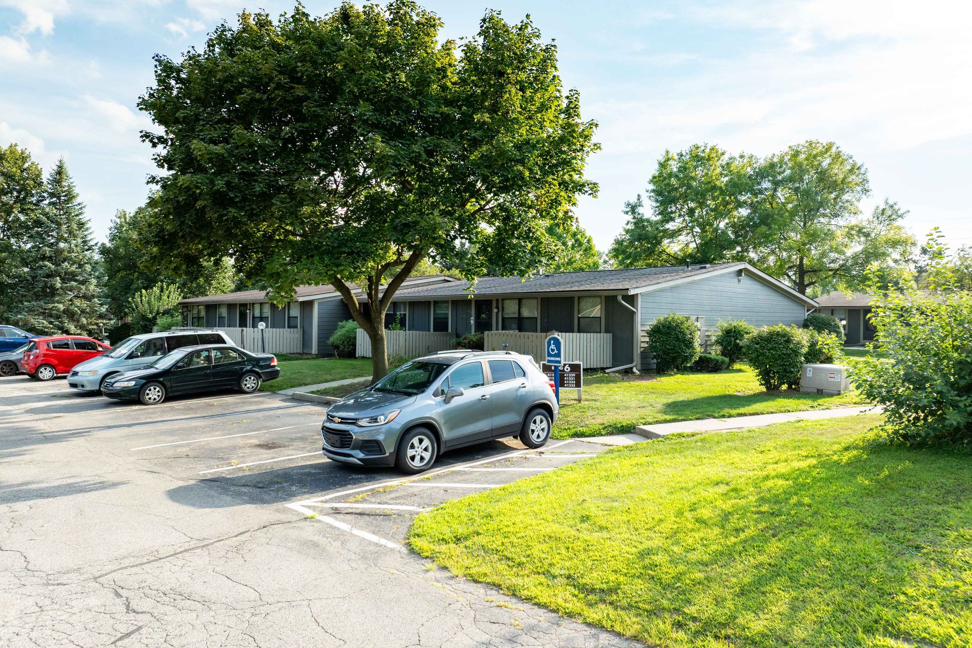 Apartment building with cars parked in front; green grass and trees.