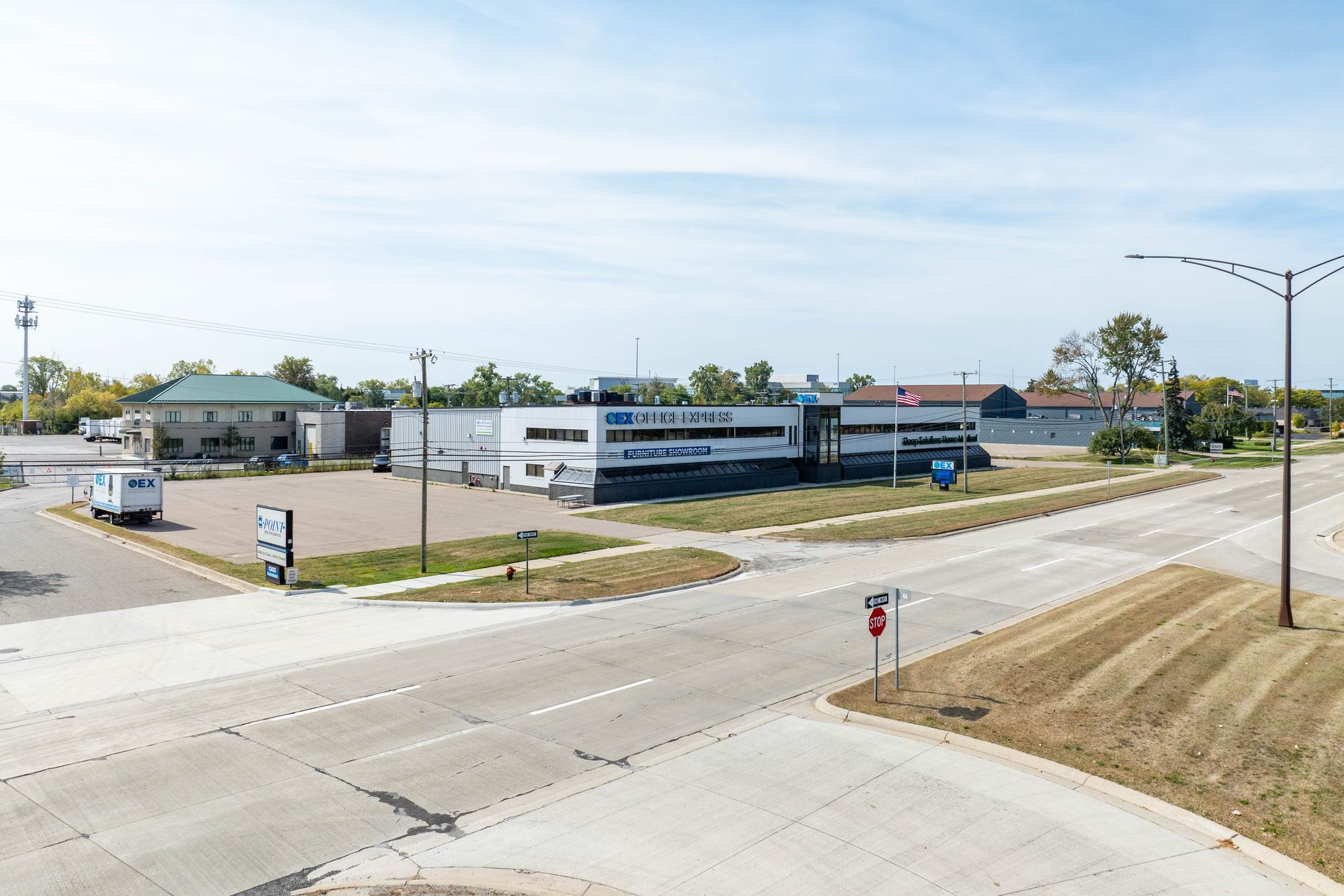 Aerial view of a commercial building with a large sign, next to a road and other buildings, on a sunny day.