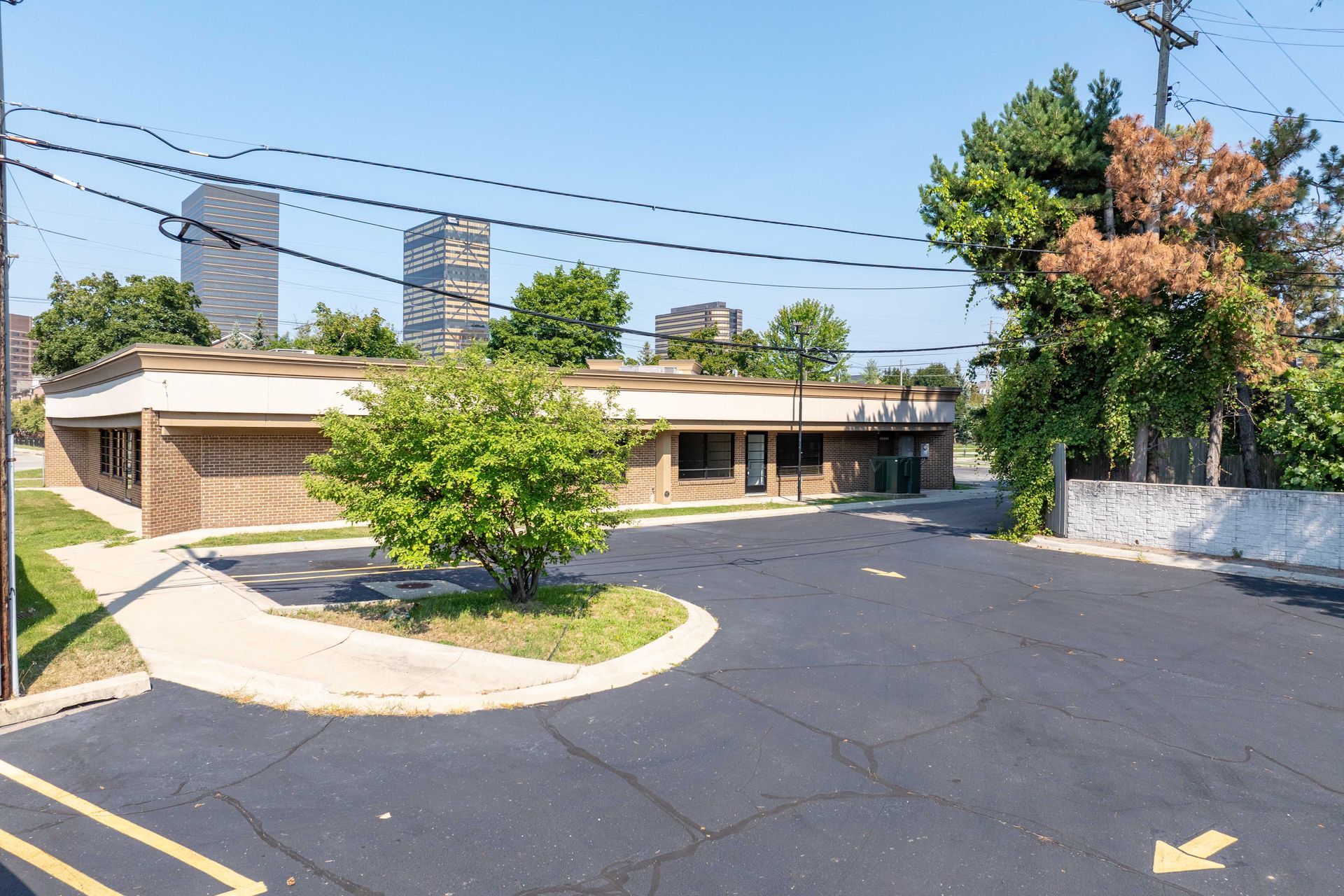 Exterior view of a one-story building with a small tree in front. Two tall buildings are in the background.