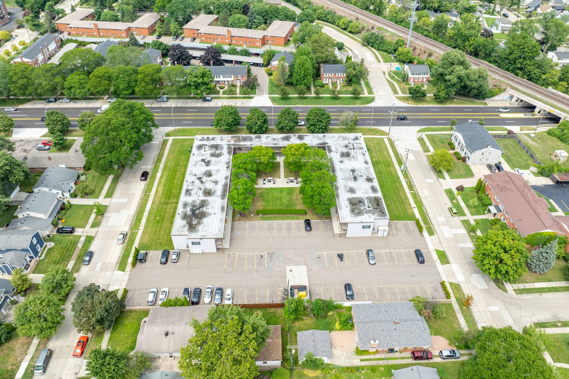 Aerial view of two white apartment buildings with central green space, parking, and surrounding residential area.