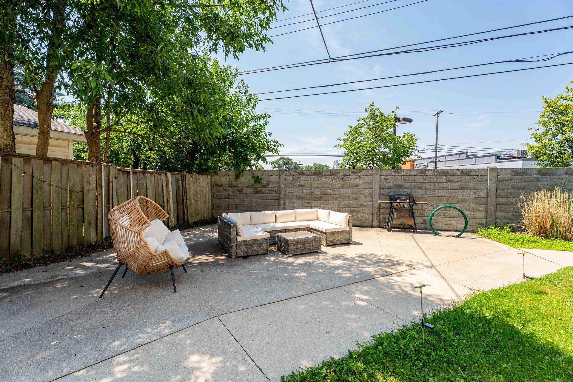 Backyard patio with wicker chair, sectional sofa, grill, and concrete walls.