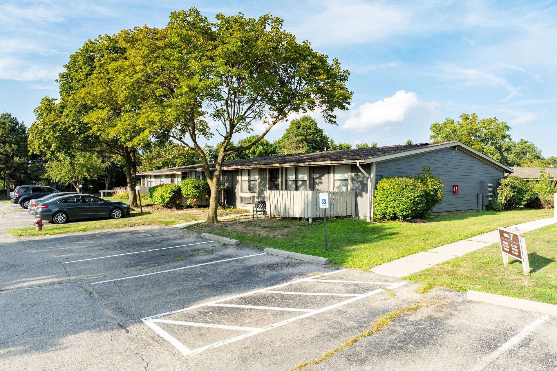 Apartment building with parking lot and trees on a sunny day.