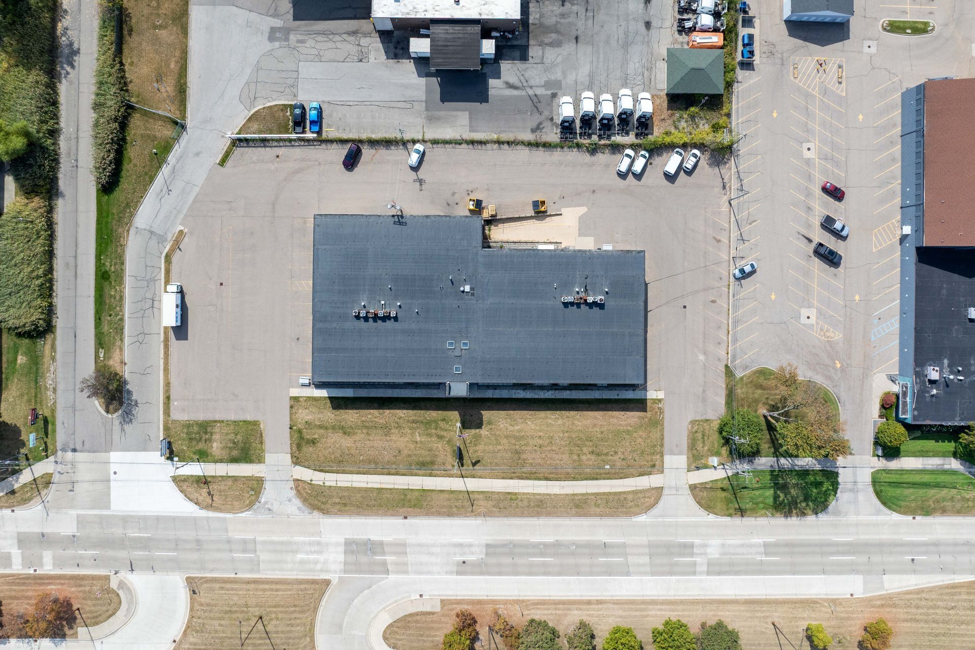 Overhead view of a commercial building with parking, street, and surrounding grass and trees.
