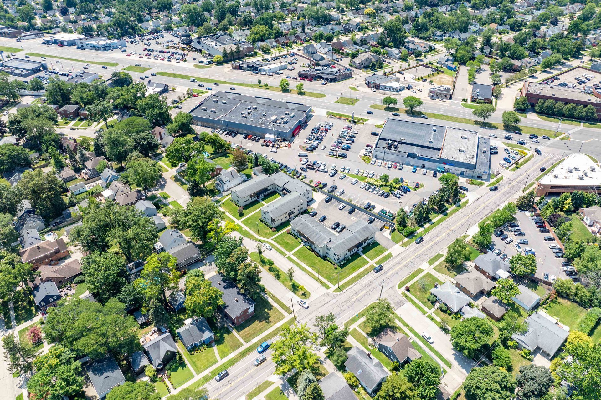 Aerial view of a town with buildings, roads, trees, and parked cars on a sunny day.
