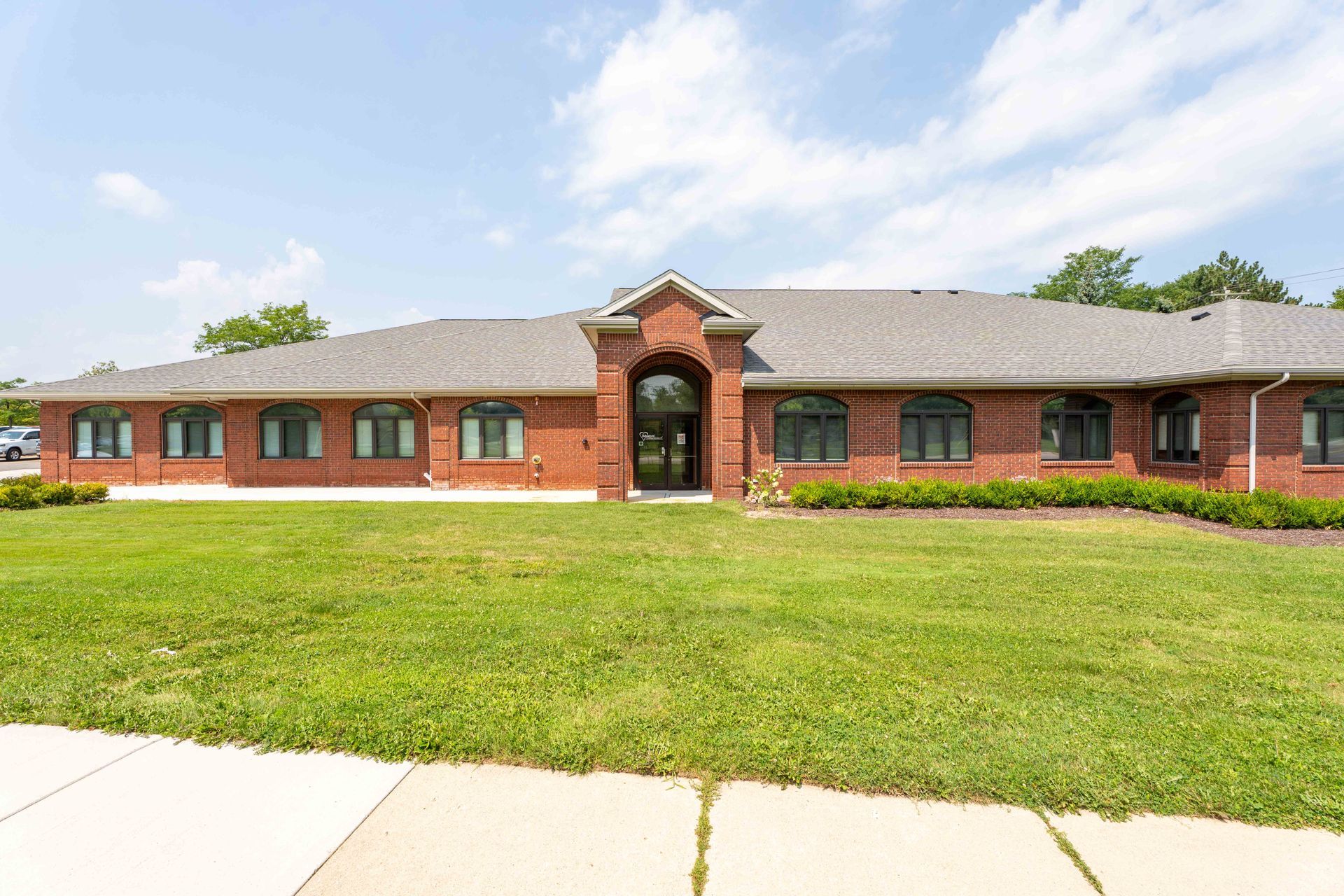 Red brick building with a grassy lawn, arched doorway, and dark windows under a blue sky.