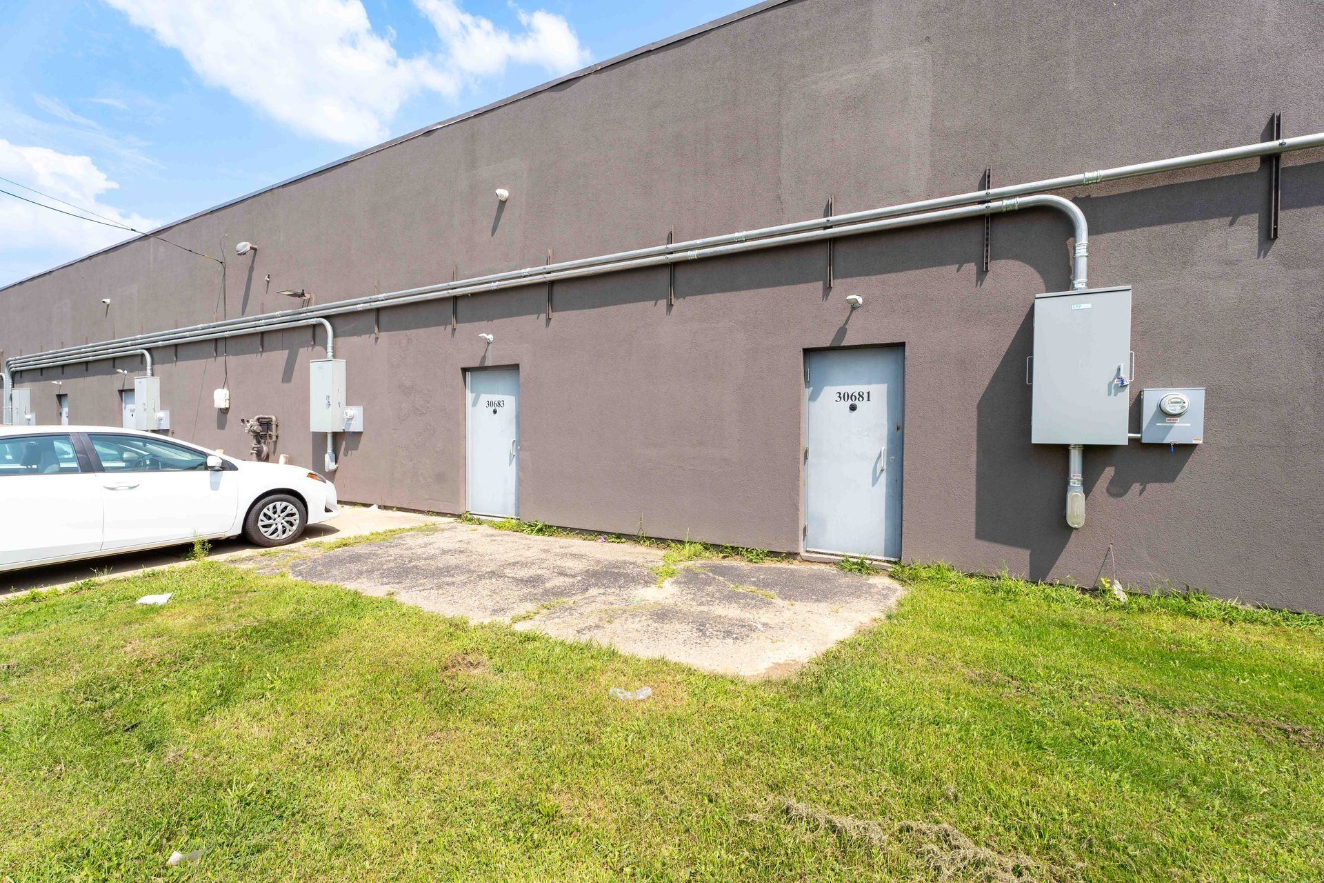 Exterior of a building with two gray doors, electrical boxes, and a white car parked on the left.
