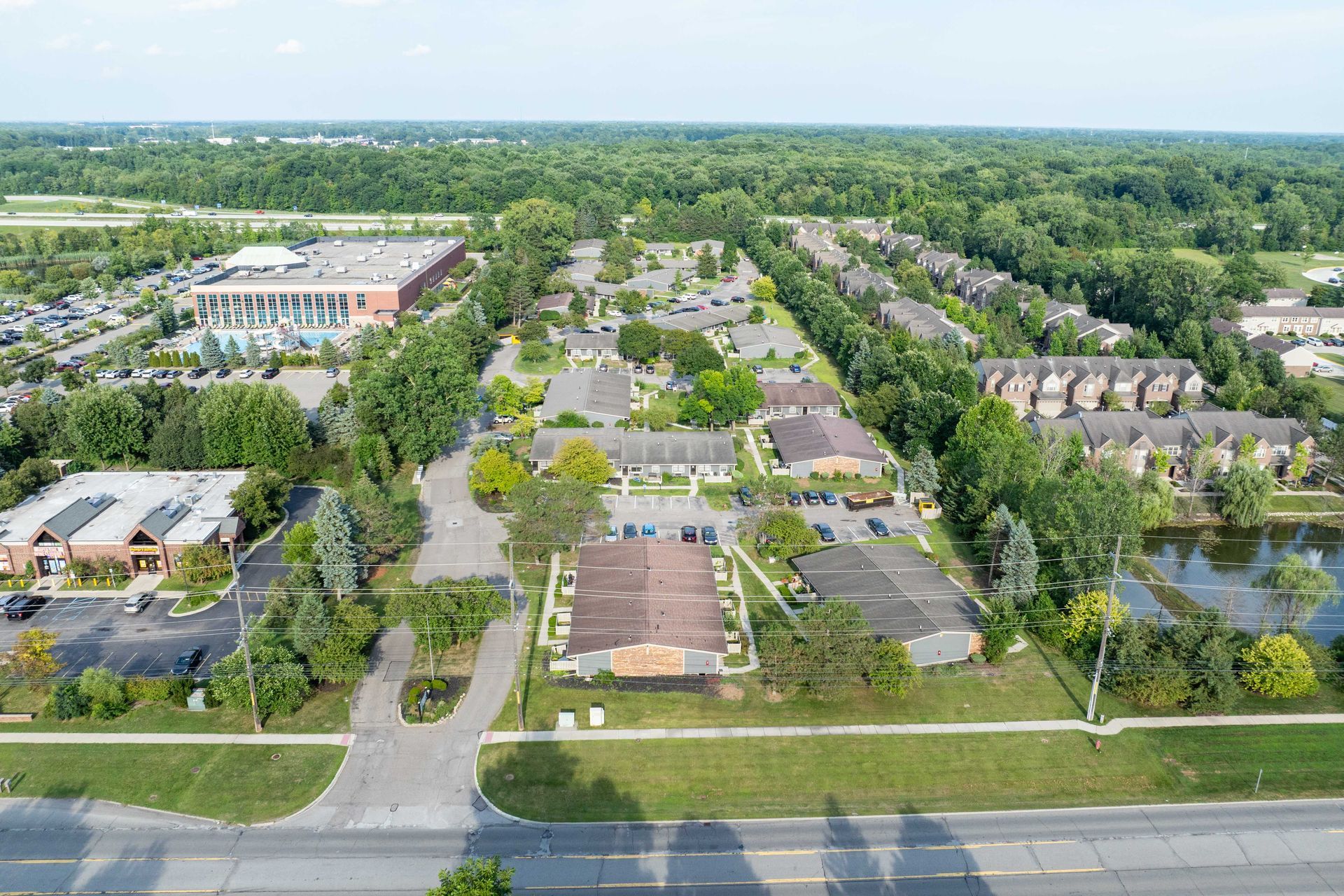 Aerial view of a residential area with buildings, trees, and a pond next to a road.