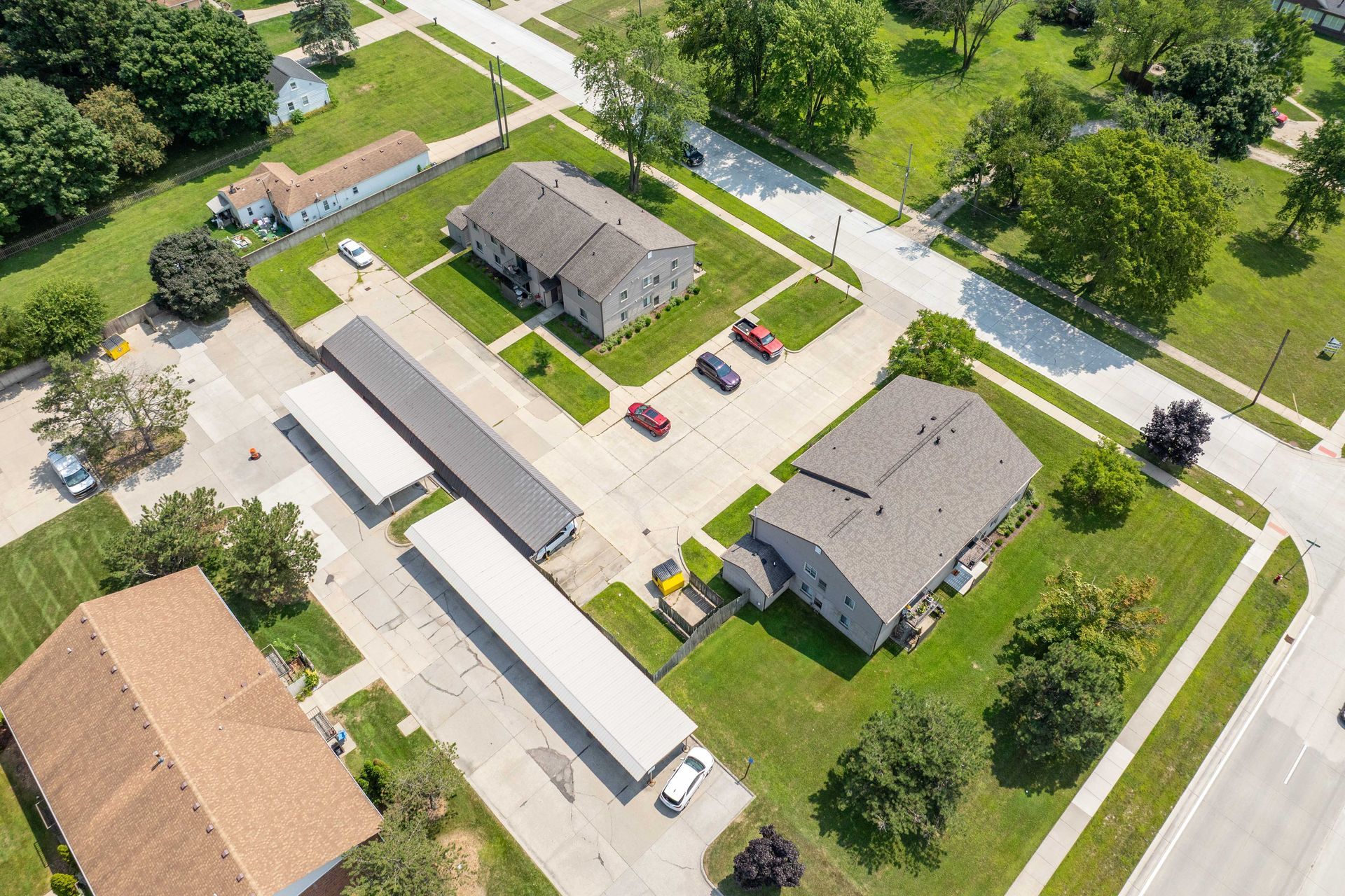 Aerial view of apartments and parking spaces with cars; green lawns and trees in a residential neighborhood.
